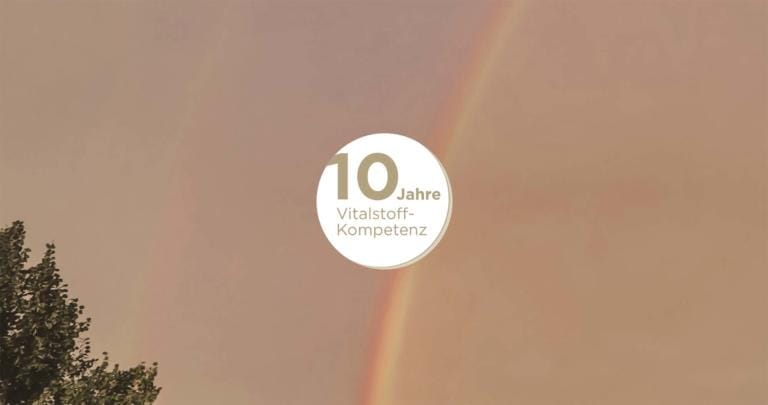 Ein schwacher doppelter Regenbogen wölbt sich über einen bewölkten Himmel mit Baumblättern unten links. In der Mitte steht auf einem weißen Kreis „10 Jahre Vitalstoff-Kompetenz“ und hebt kingnature Stories hervor.