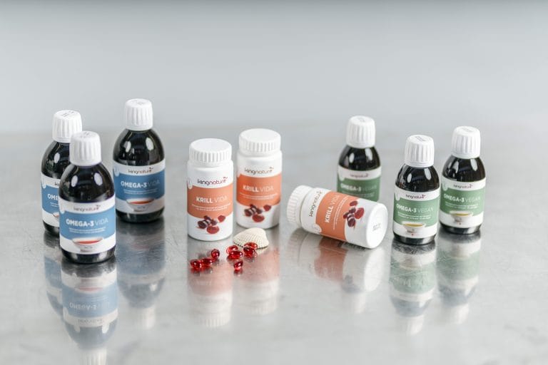 Auf einer reflektierenden Oberfläche werden mehrere Flaschen und Behälter mit Omega-3 Vegan- und Krill Vida-Nahrungsergänzungsmitteln präsentiert, in der Mitte sind veganfreundliche rote Kapseln und weiße Tabletten verstreut.