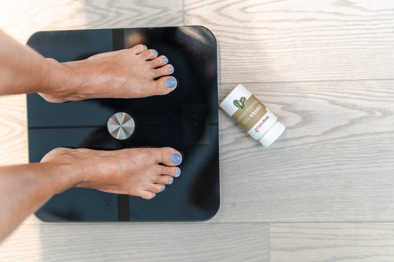 Eine Person mit blauen Zehennägeln steht auf einer digitalen Waage neben einem Deostick und einer Packung Grünem Kaffee auf einem hellen Holzboden.