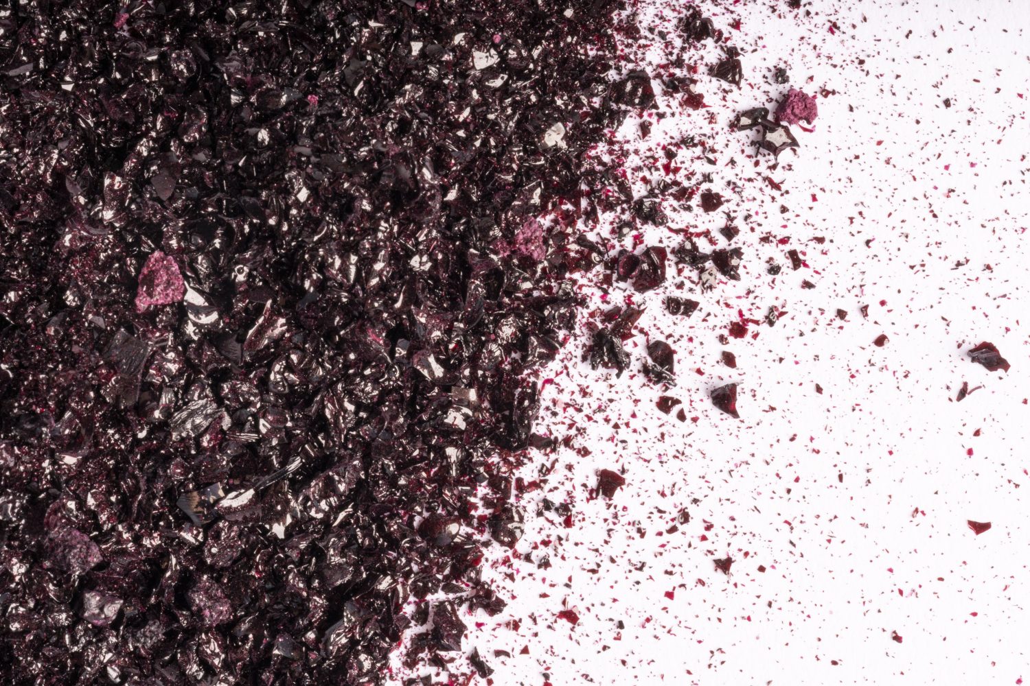 Zerkleinertes dunkelviolettes Pulver, das über eine weiße Fläche gestreut wird, konzentriert auf der linken Seite und allmählich nach rechts auslaufend, wodurch ein strukturierter, dynamischer Effekt entsteht.