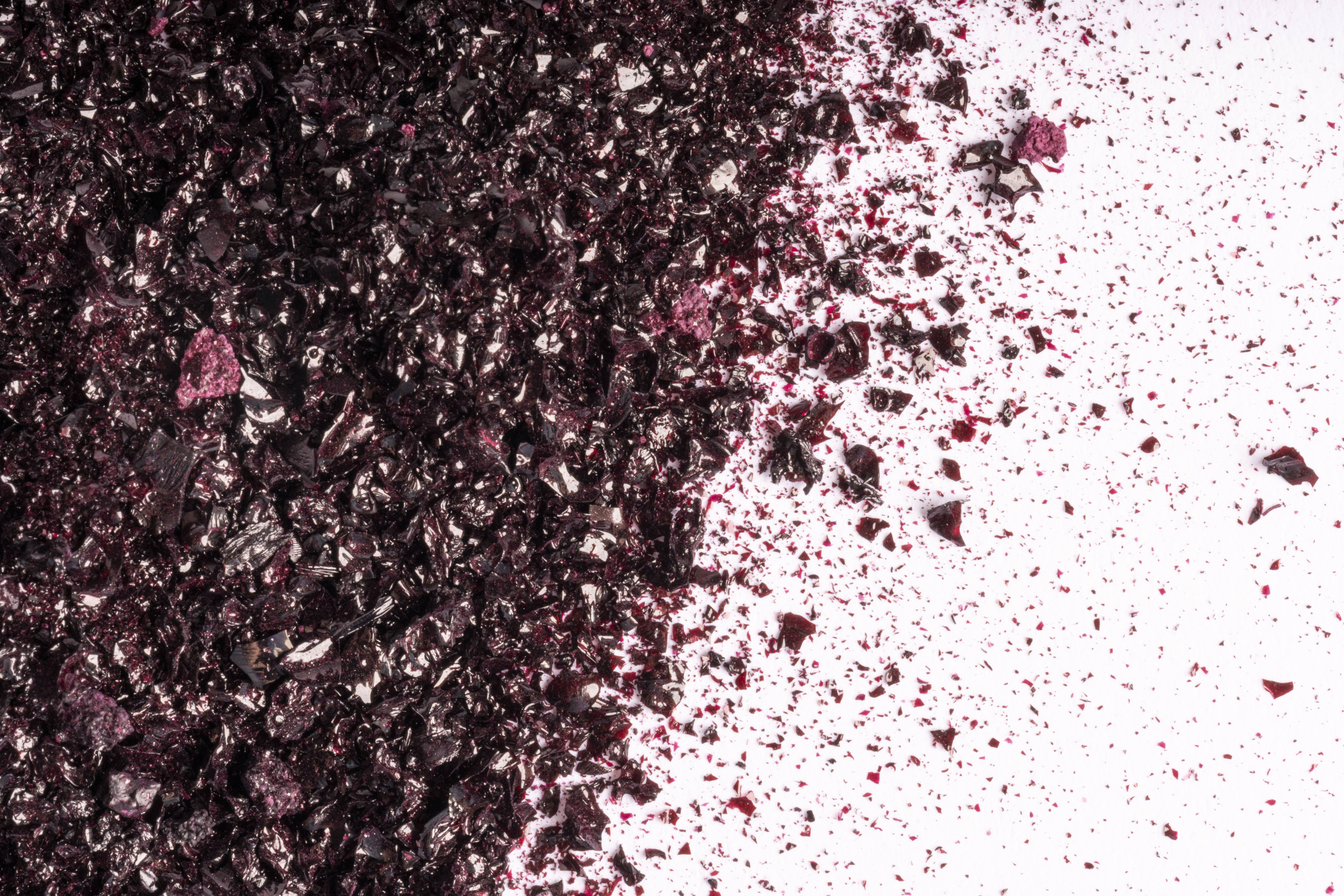 Zerkleinertes dunkelviolettes Pulver, das über eine weiße Fläche gestreut wird, konzentriert auf der linken Seite und allmählich nach rechts auslaufend, wodurch ein strukturierter, dynamischer Effekt entsteht.