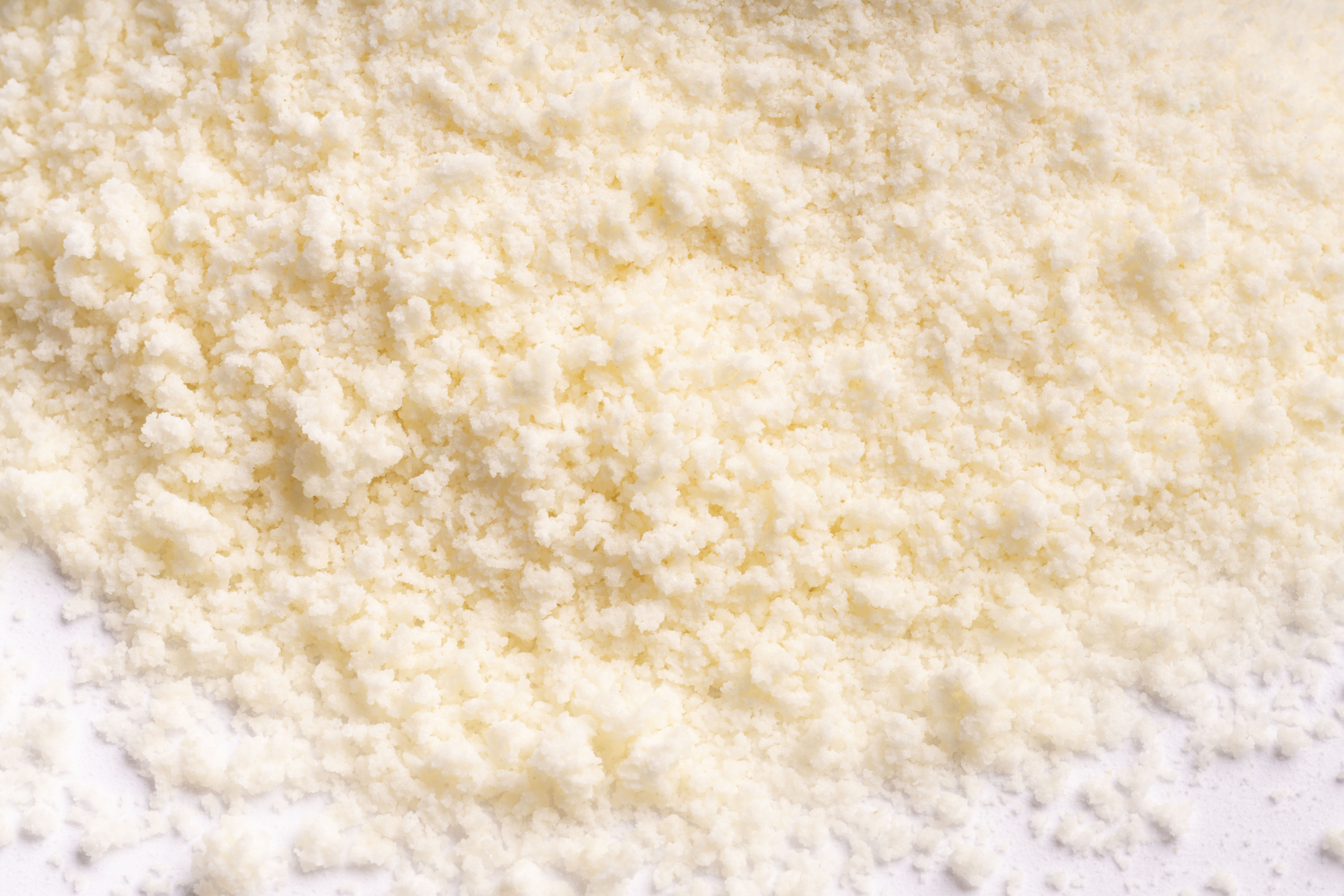 Nahaufnahme eines Haufens fein geriebenen weißen Käses, der auf eine weiße Fläche gestreut ist.