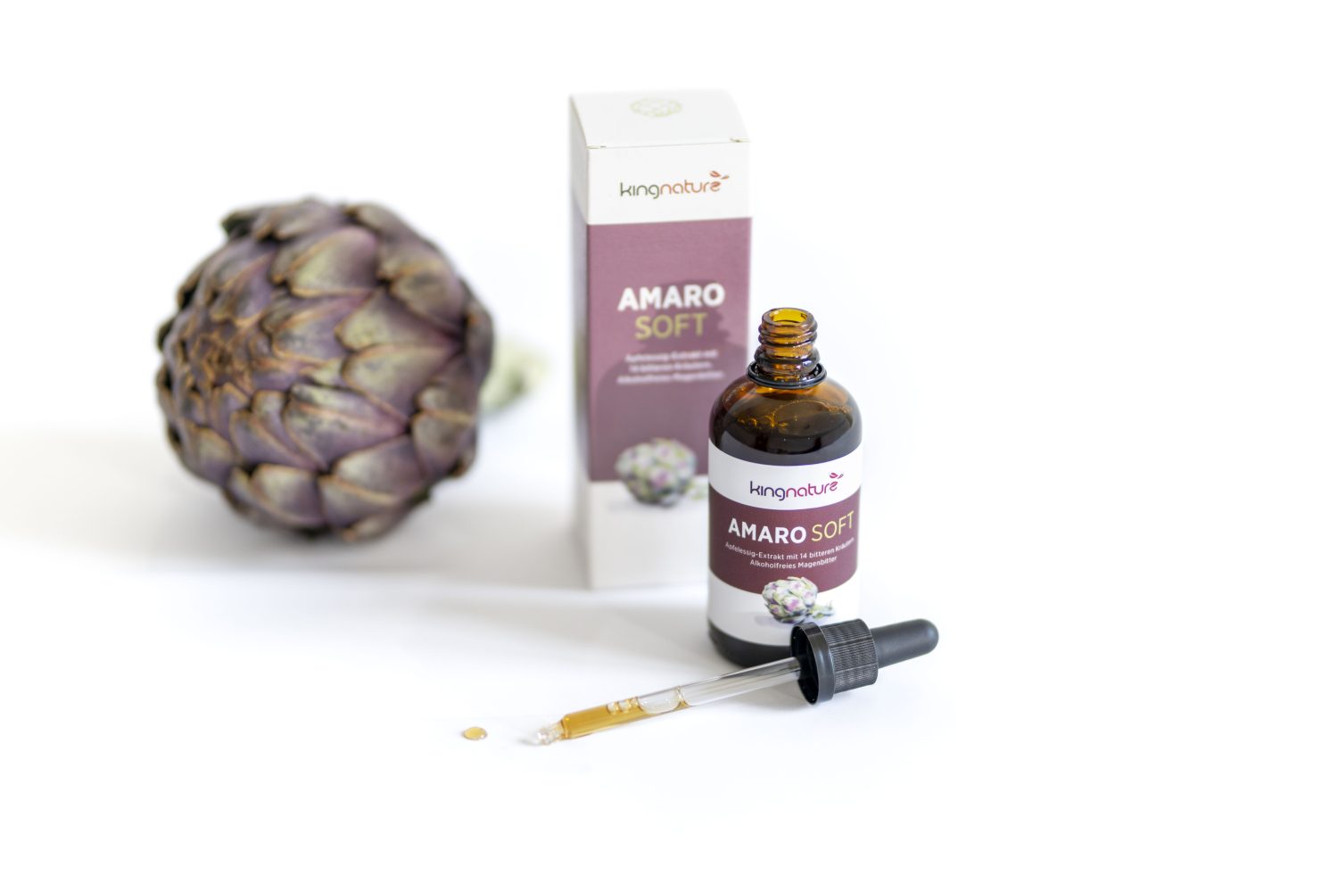 Eine Flasche des pflanzlichen Nahrungsergänzungsmittels Amaro Soft mit einem Tropfer, der Verpackungsschachtel und einer ganzen Artischocke auf weißem Hintergrund. Der Tropfer hat ein paar Tropfen Flüssigkeit neben der Flasche.