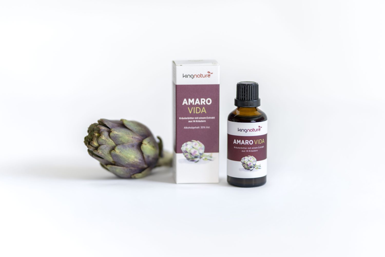 Eine Flasche und eine Schachtel mit der Aufschrift AMARO VIDA und einer violetten Artischocke stehen neben einer frischen Artischocke, alles vor einem weißen Hintergrund.