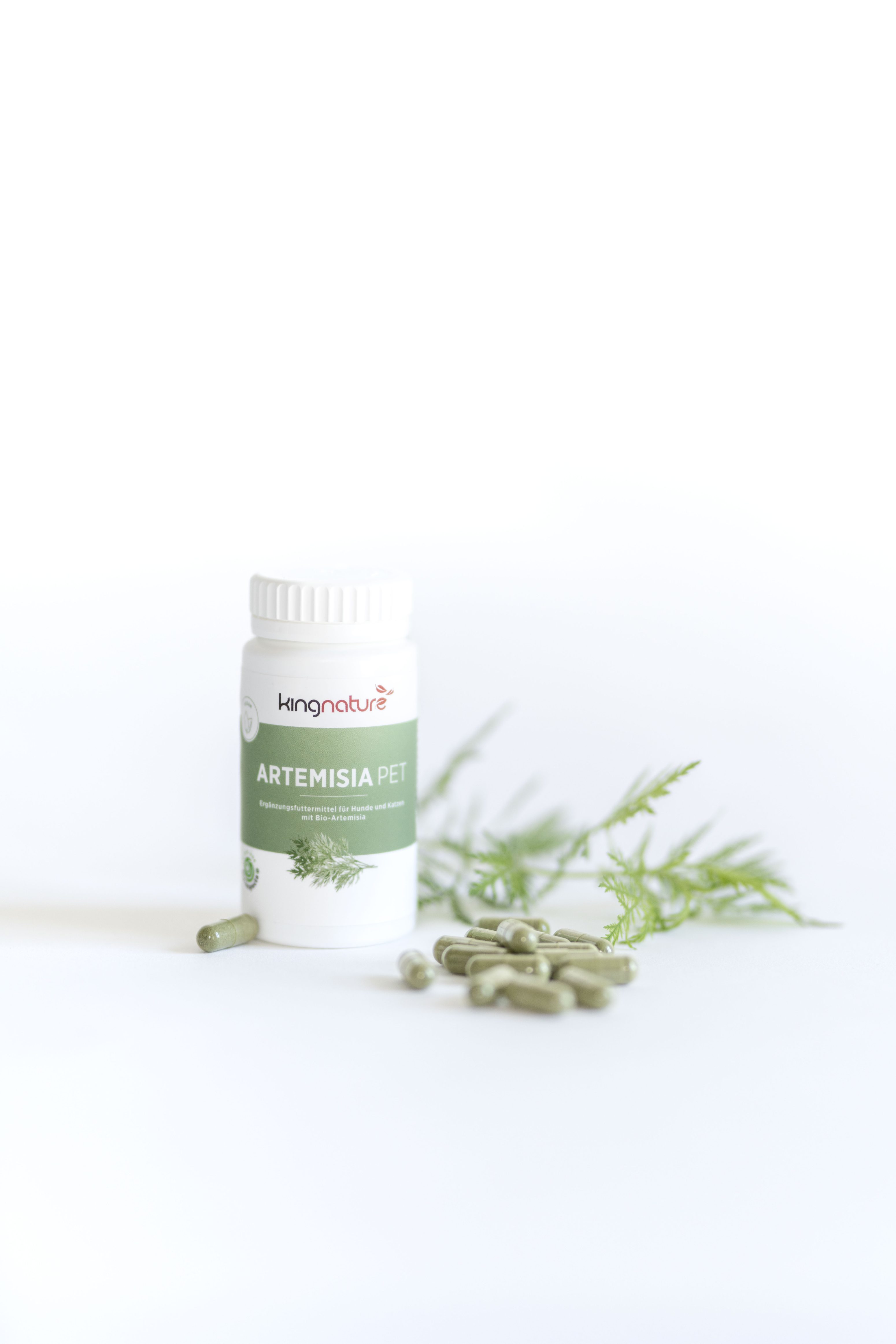 Ein weißes Fläschchen mit der Aufschrift Artemisia Pet, aus dem grüne Kapseln austreten, neben einem Zweig mit grünen Blättern, auf einem sauberen weißen Hintergrund.