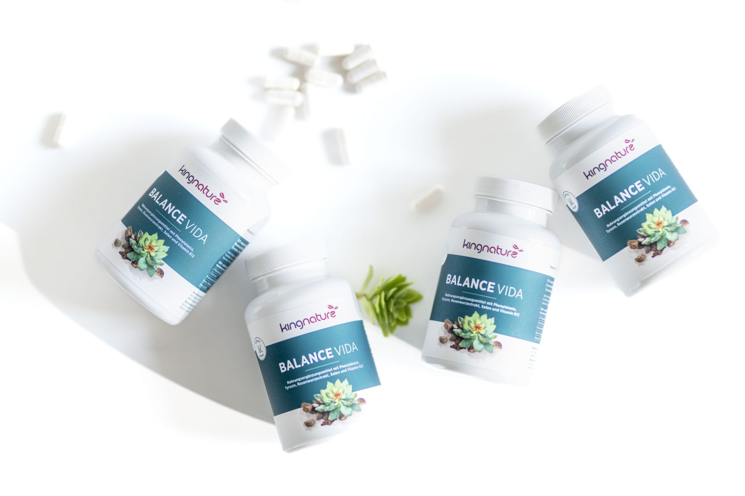Vier weiße Flaschen mit der Aufschrift Balance Vida von kingnature stehen auf einer weißen Fläche, daneben befinden sich einige weiße Kapseln und eine kleine grüne Sukkulentenpflanze.