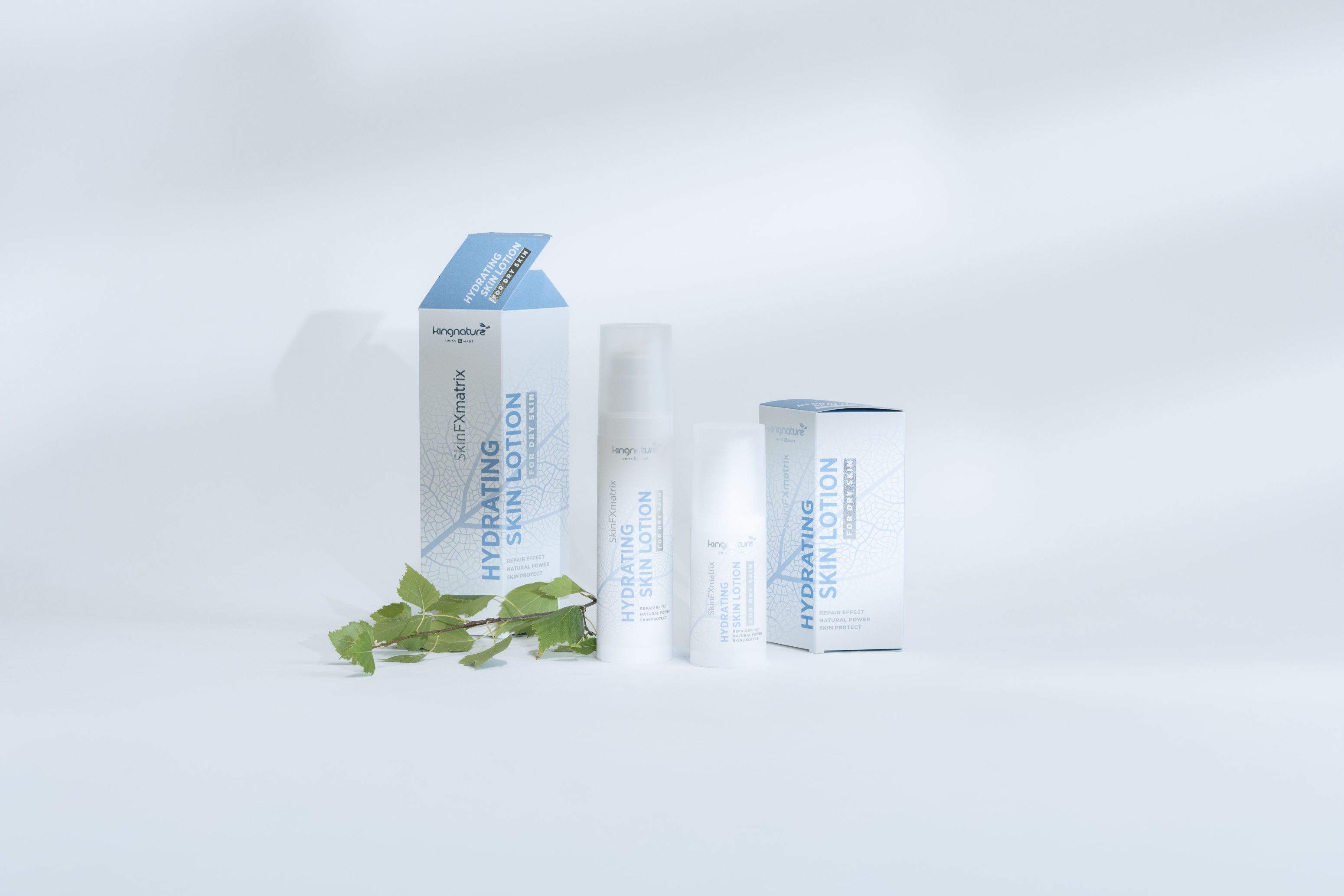 Eine Flasche Hydrating Skin Lotion steht neben ihrer blau-weißen Verpackung, daneben eine weitere Flasche und kleine grüne Blätter, alles vor einem hellen, weichen Hintergrund.