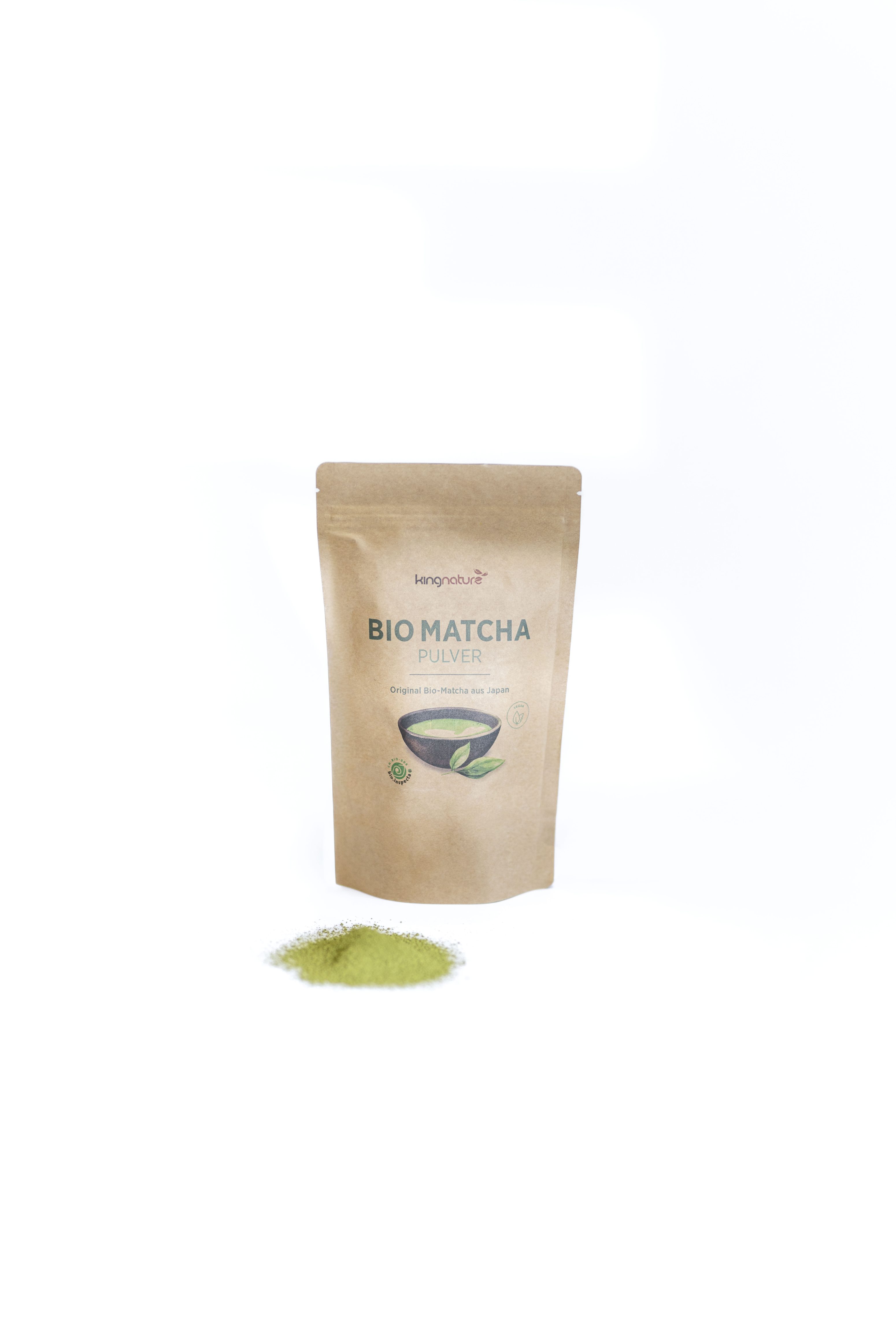 Ein brauner Kraftpapierbeutel mit der Aufschrift Bio Matcha Pulver steht aufrecht mit einem kleinen Haufen grünen Matcha-Pulvers vor einem weißen Hintergrund.