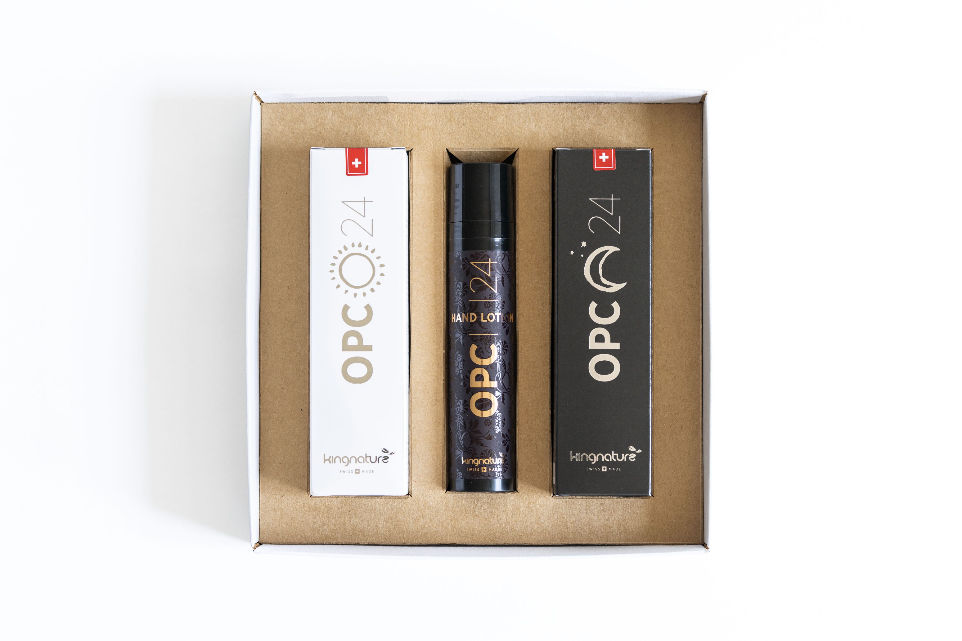 Eine Pappschachtel, die drei Produkte enthält: zwei rechteckige Schachteln mit der Aufschrift "OPC 24" auf der linken und rechten Seite und eine Flasche in der Mitte mit der Aufschrift "OPC 24 Hand Lotion" von kingnature, alles auf weißem Hintergrund.