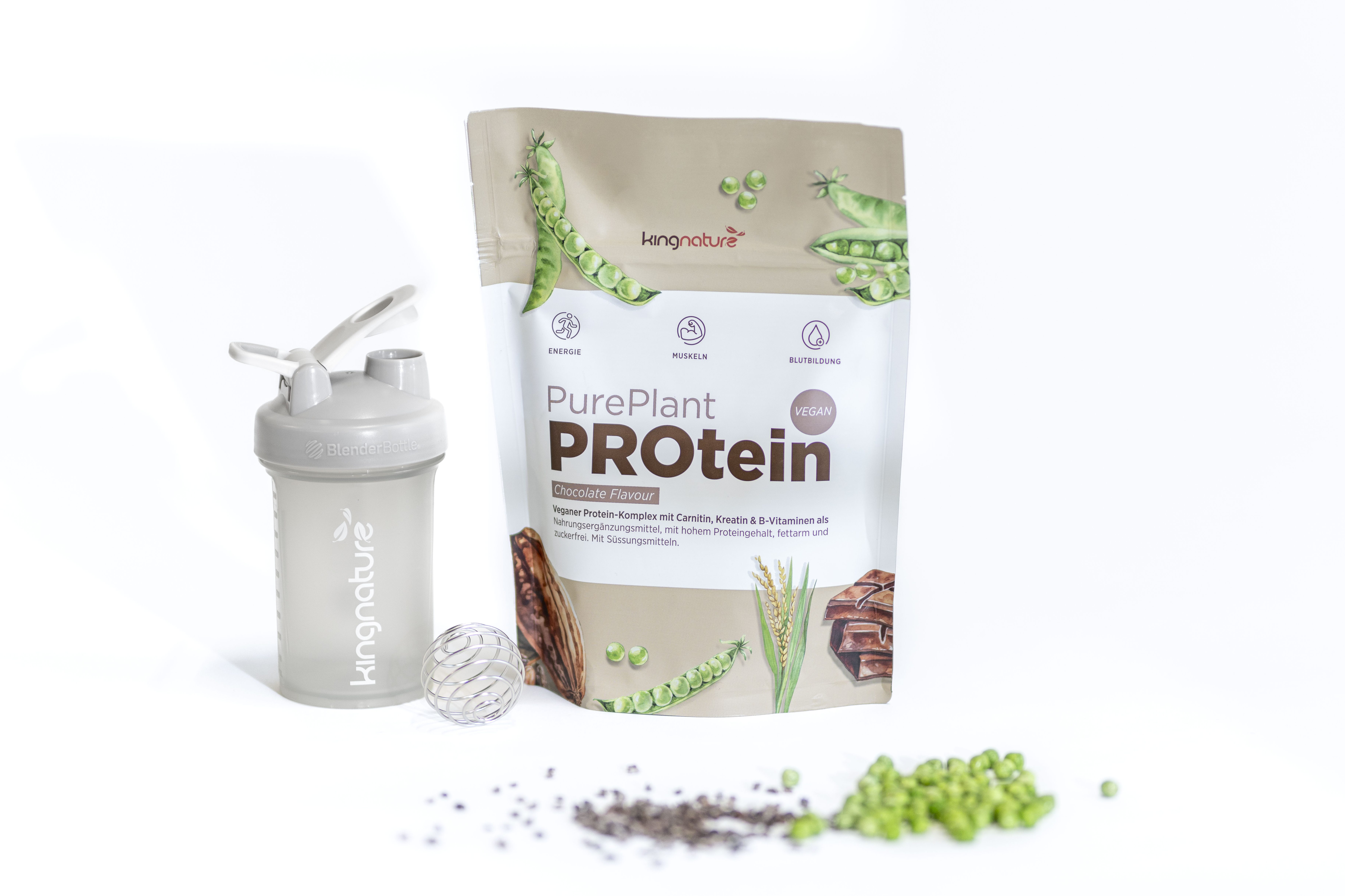 Eine Packung Kingnature PurePlant PROtein Pulver steht neben einer Schüttelflasche. Davor befinden sich Samen, grüne Erbsen und ein Messlöffel, alles auf weißem Hintergrund verstreut.