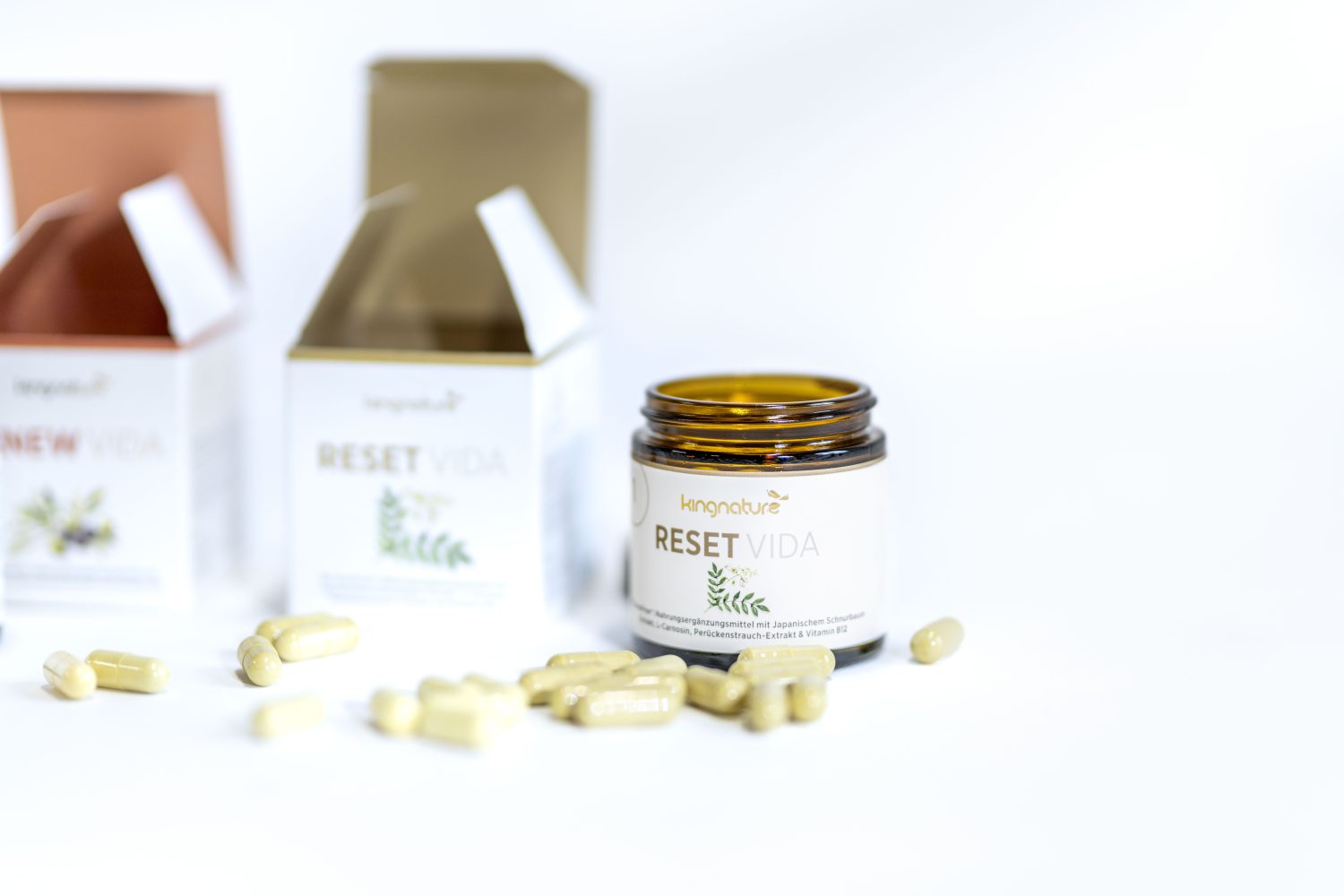 Ein geöffnetes braunes Ergänzungsglas mit der Aufschrift RESET VIDA und verstreuten Kapseln, daneben zwei geöffnete Schachteln mit der gleichen Aufschrift, auf weißem Hintergrund.