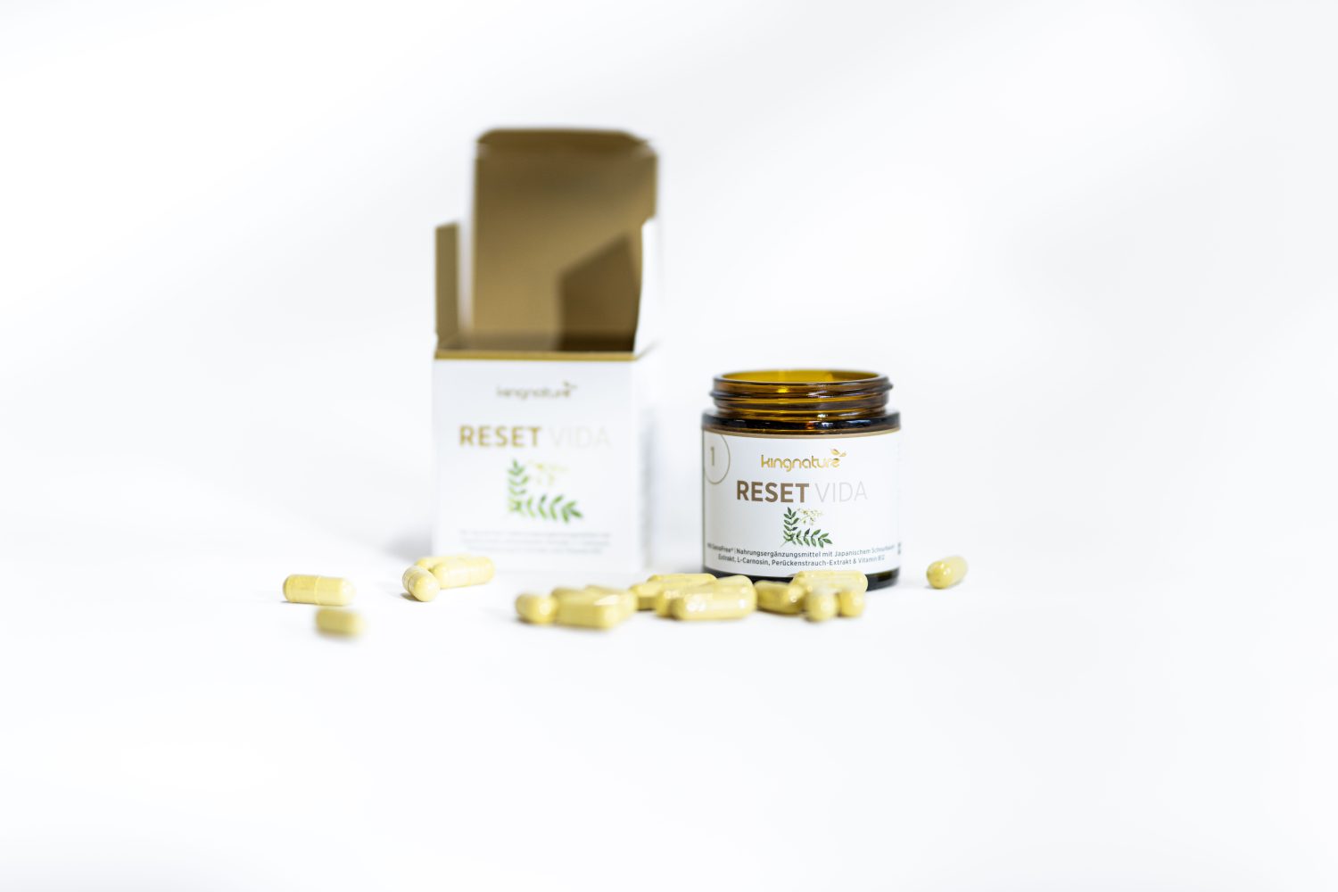 Ein braunes Glasgefäß und eine Pappschachtel mit der Aufschrift Reset Vida mit mehreren gelben Kapseln, die auf weißem Hintergrund verstreut sind. Das Glas ist geöffnet und die Schachtel ist teilweise geöffnet.