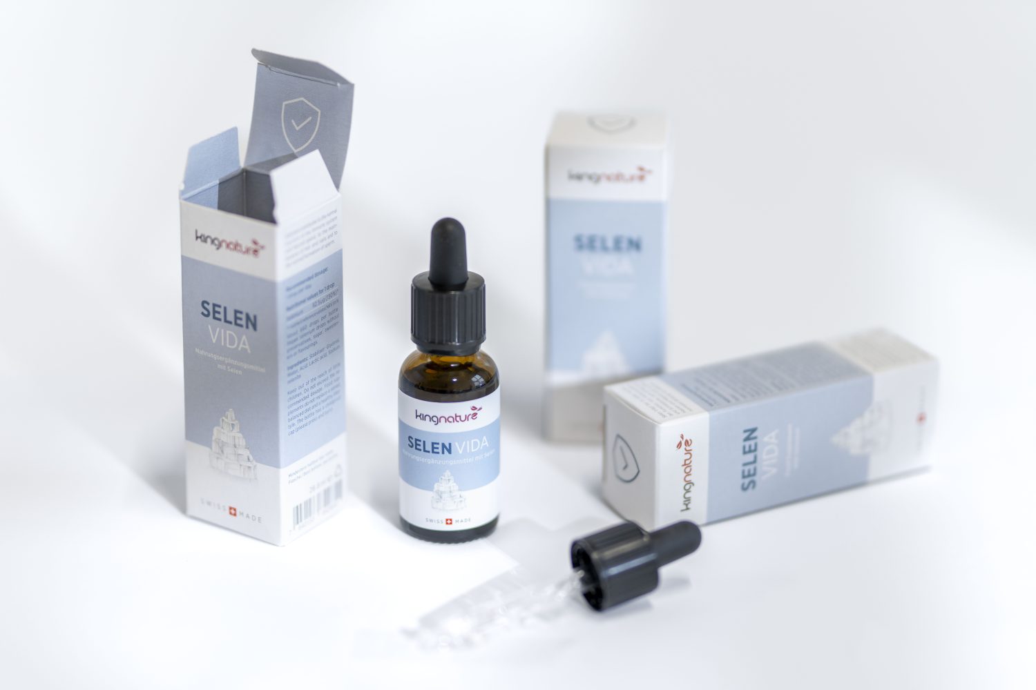 Eine Flasche des flüssigen Nahrungsergänzungsmittels Kenguruz Selen Vida mit einer Pipette, die neben den Verpackungsschachteln auf weißem Hintergrund ausgestellt ist. Eine Schachtel ist geöffnet, und der Tropfer ist davor platziert.