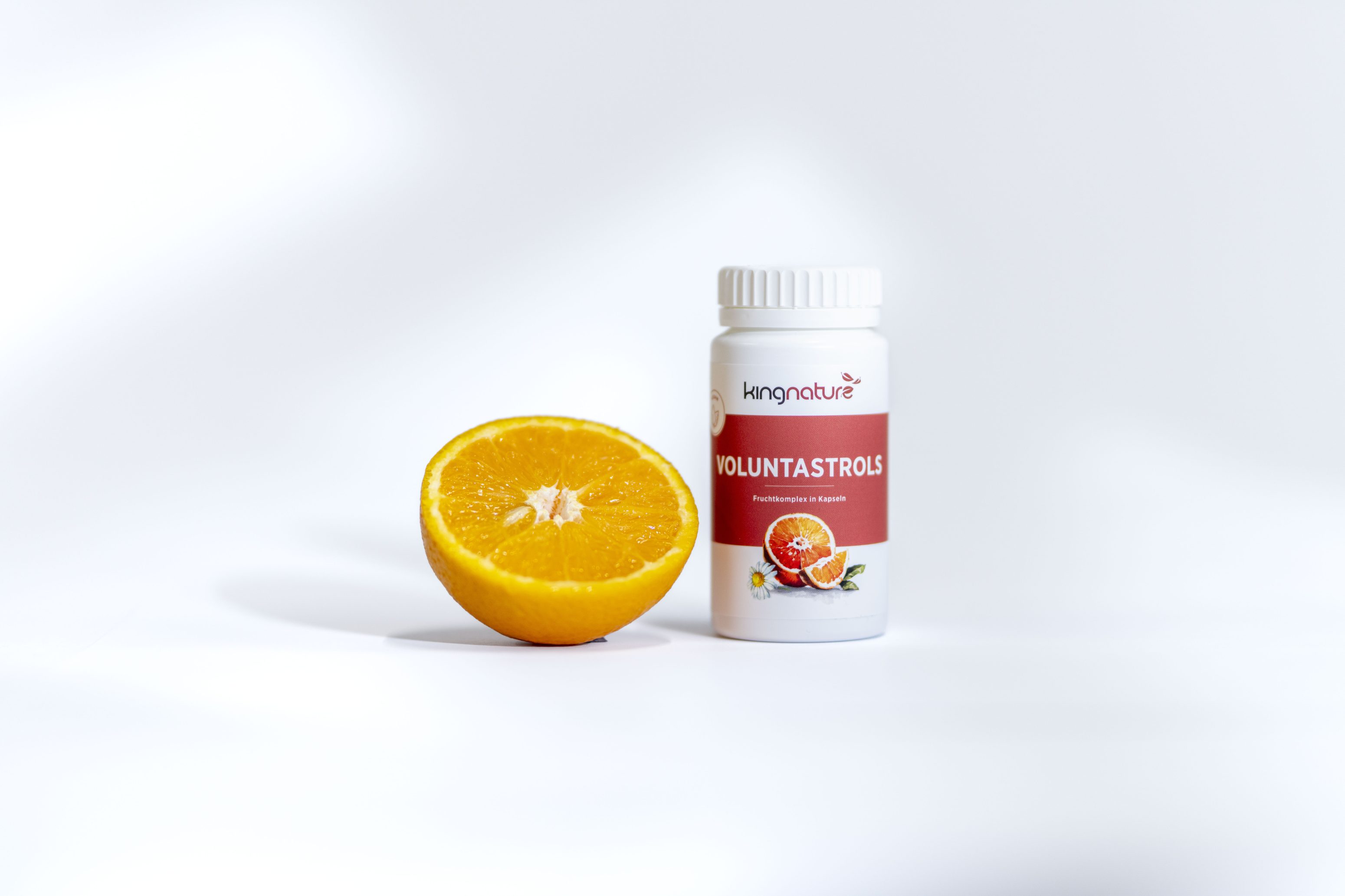 Eine halbierte Orange steht neben einer weißen Flasche mit der Aufschrift Voluntastrols by Living Nature, die eine orangefarbene Grafik auf weißem Hintergrund zeigt.