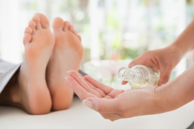 In der alviva Naturheilpraxis gießt sich eine Person Öl in die Hände und bereitet sich auf eine Fußmassage vor. Im Hintergrund liegt eine weitere Person mit freiliegenden Füßen da und ist bereit zur Entspannung.
