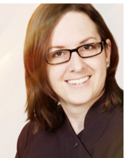 Sonja Grünenfelder von Farfallina Kosmetik, mit schulterlangen braunen Haaren und Brille, lächelt in einem dunklen Top vor hellem Hintergrund in die Kamera.
