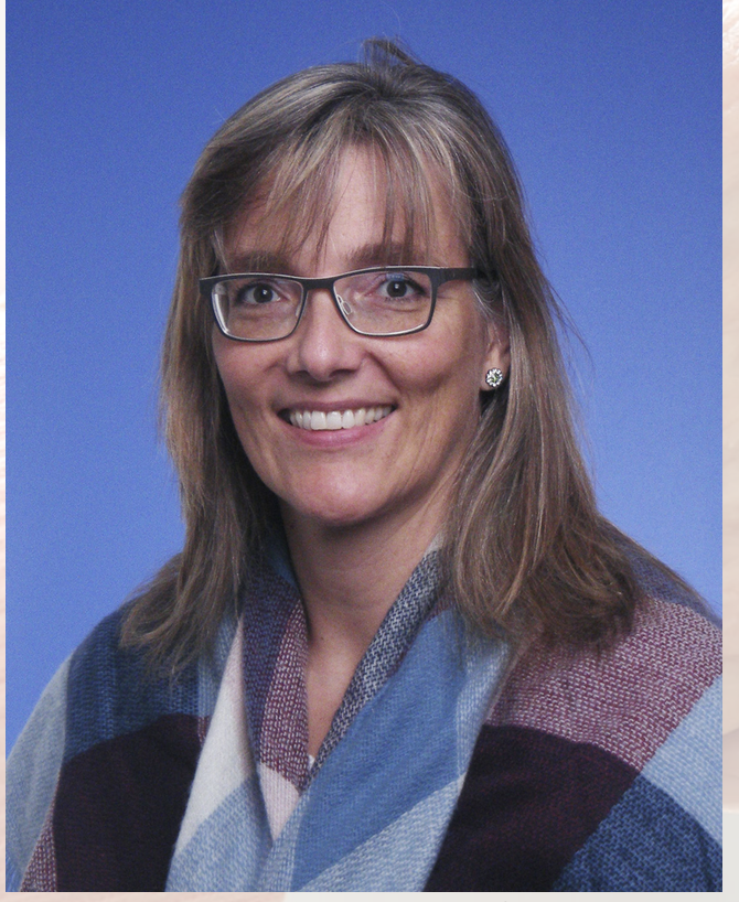 Barbara Roth, von der Beandcare GmbH, lächelt in die Kamera. Sie hat glattes, schulterlanges hellbraunes Haar und eine Brille. Sie trägt einen karierten Schal und ein blaues Oberteil mit einem blauen Hintergrund im Hintergrund.