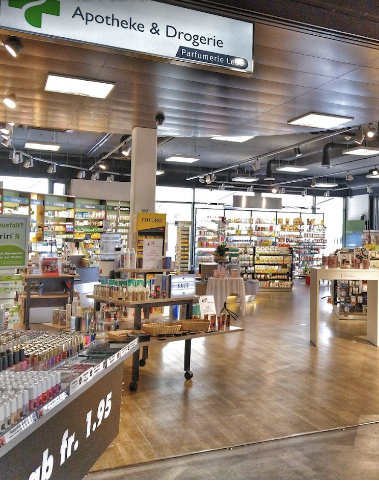 Eine gut beleuchtete Apotheke und Drogerie mit Regalen, die mit verschiedenen Gesundheits-, Schönheits- und Körperpflegeprodukten bestückt sind. Auf einem Schild über der Apotheke & Drogerie steht "Apotheke & Drogerie", und ein automatisch gespeicherter Entwurf hebt die angebotenen Kosmetika und Verkaufsartikel im Eingangsbereich hervor.