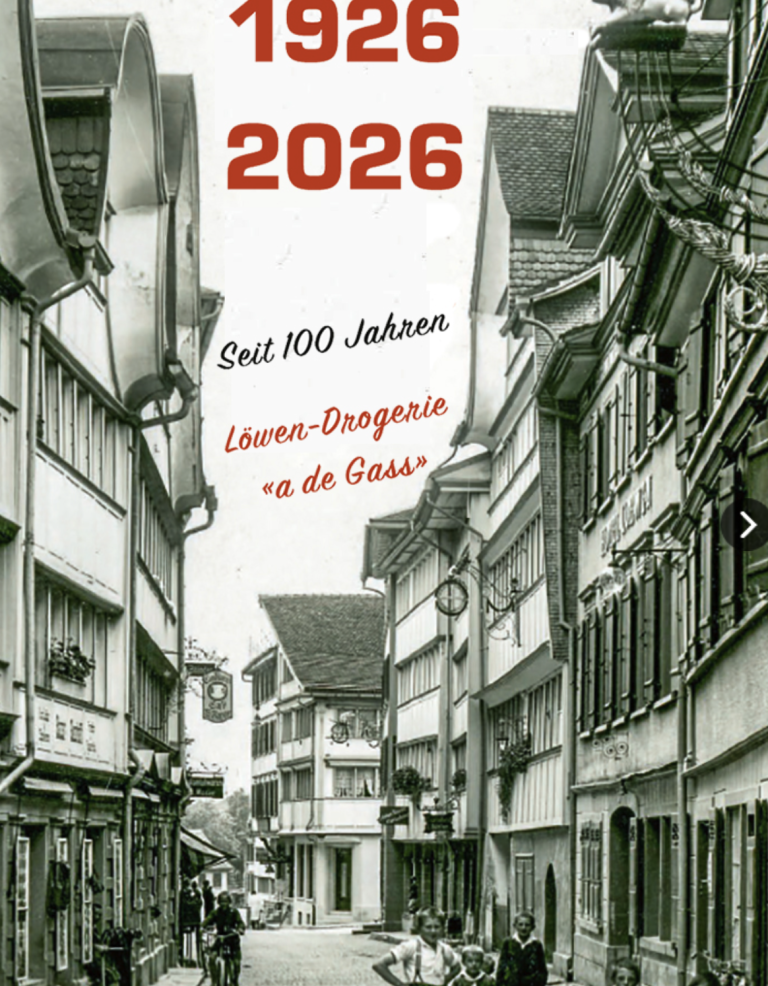 Schwarz-Weiß-Foto einer engen europäischen Straße mit alten Gebäuden. Der Text lautet: 1926 2026 Automatisch gespeicherter Entwurf - Seit 100 Jahren Löwen-Drogerie a de Gass, anlässlich eines Jahrhunderts von 1926 bis 2026.