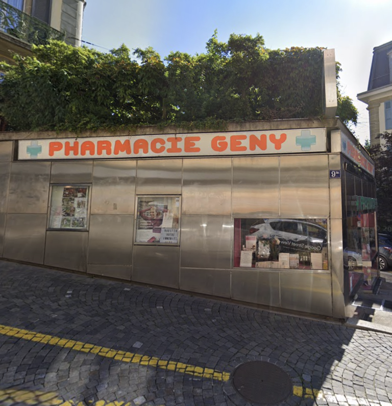 Eine Eckapotheke mit dem Namen PHARMACIE GENY mit einer Metallfassade und großen Fenstern, gelegen an einer Kopfsteinpflasterstraße. Ein automatisch gespeicherter Entwurf zeigt einen gespeicherten Entwurf im Fenster an. Auf dem Dach über dem Eingang wachsen Pflanzen.