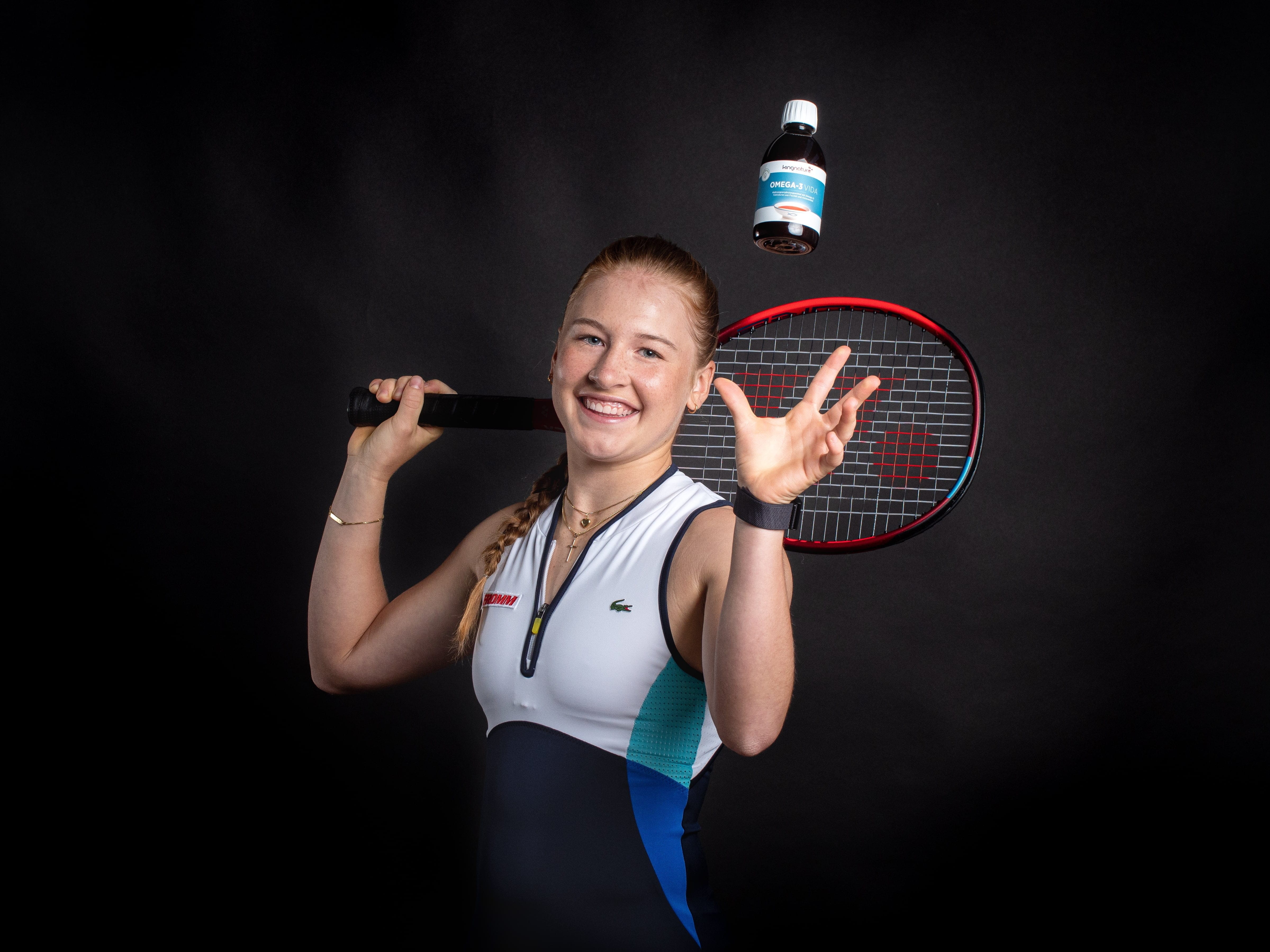 Eine lächelnde Tennisspielerin hält einen Schläger über ihrer Schulter und wirft mit der anderen Hand vor einem dunklen Hintergrund eine kleine Flasche mit der Aufschrift „Pure Encapsulations Supplement“.
