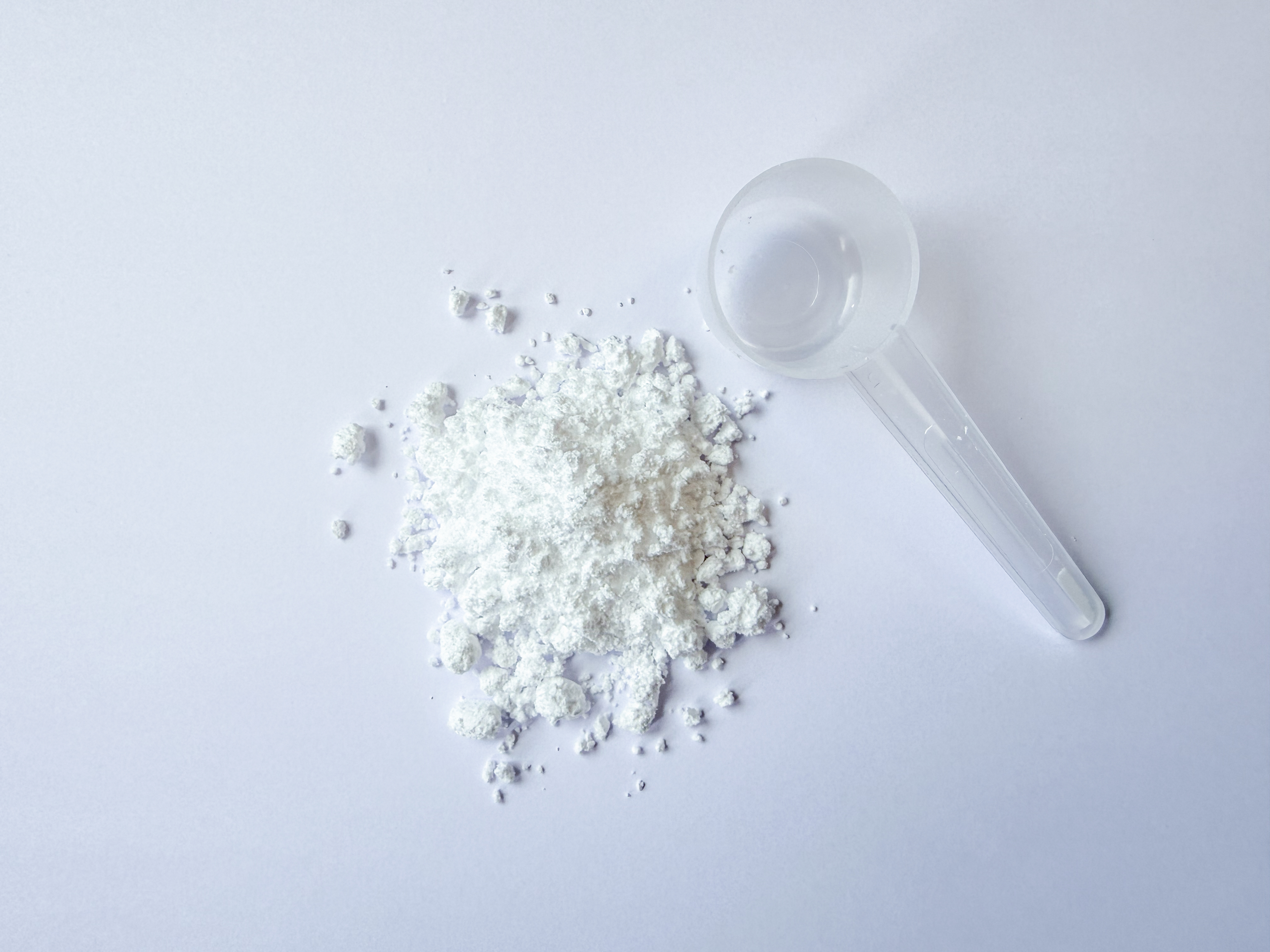 Auf einer schlichten weißen Fläche liegt eine kleine, durchsichtige Plastikschaufel neben einem Haufen feinen weißen Creatine Vida-Pulvers.