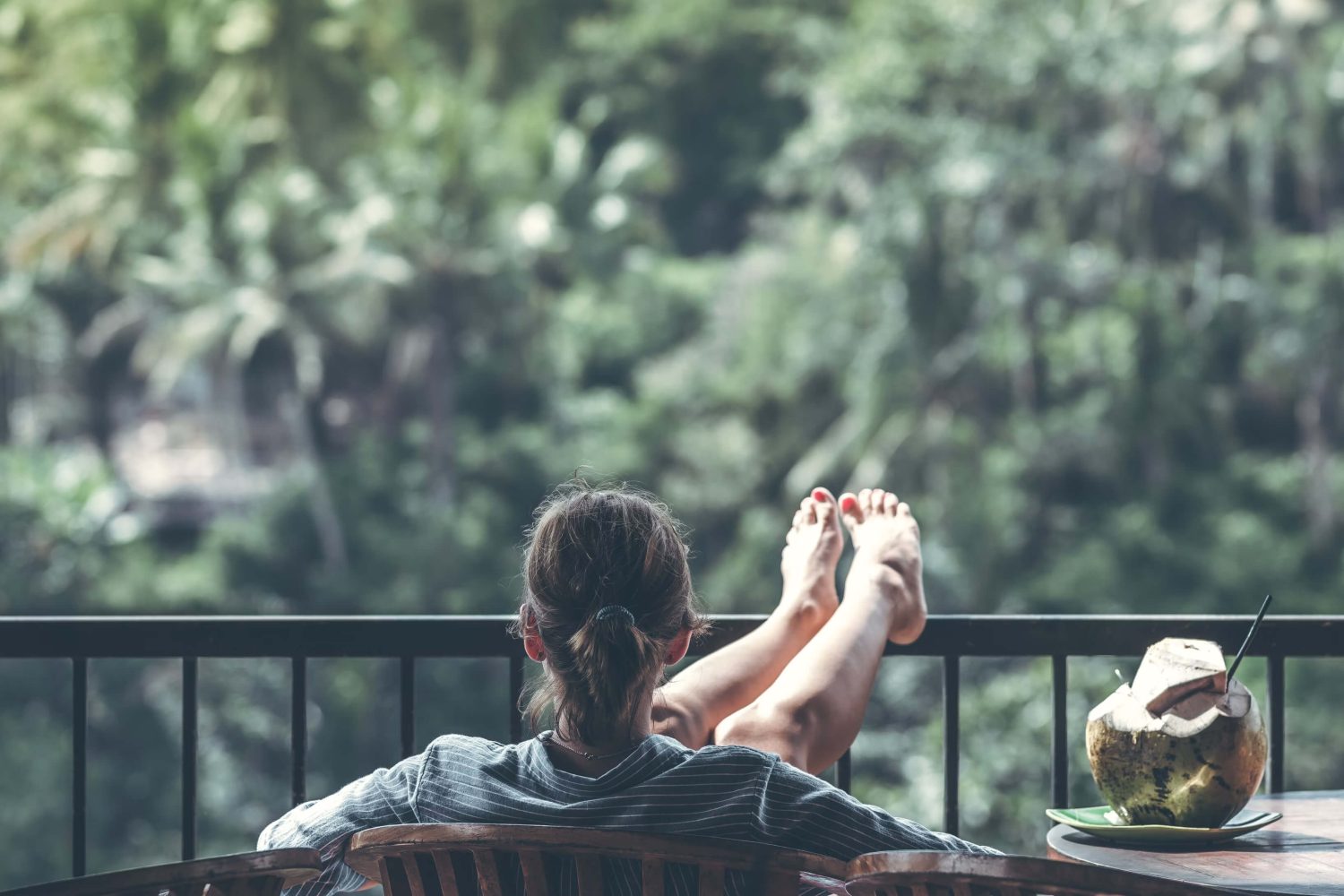Eine Frau sitzt mit hochgelegten Beinen mit Blick auf die Natur draußen