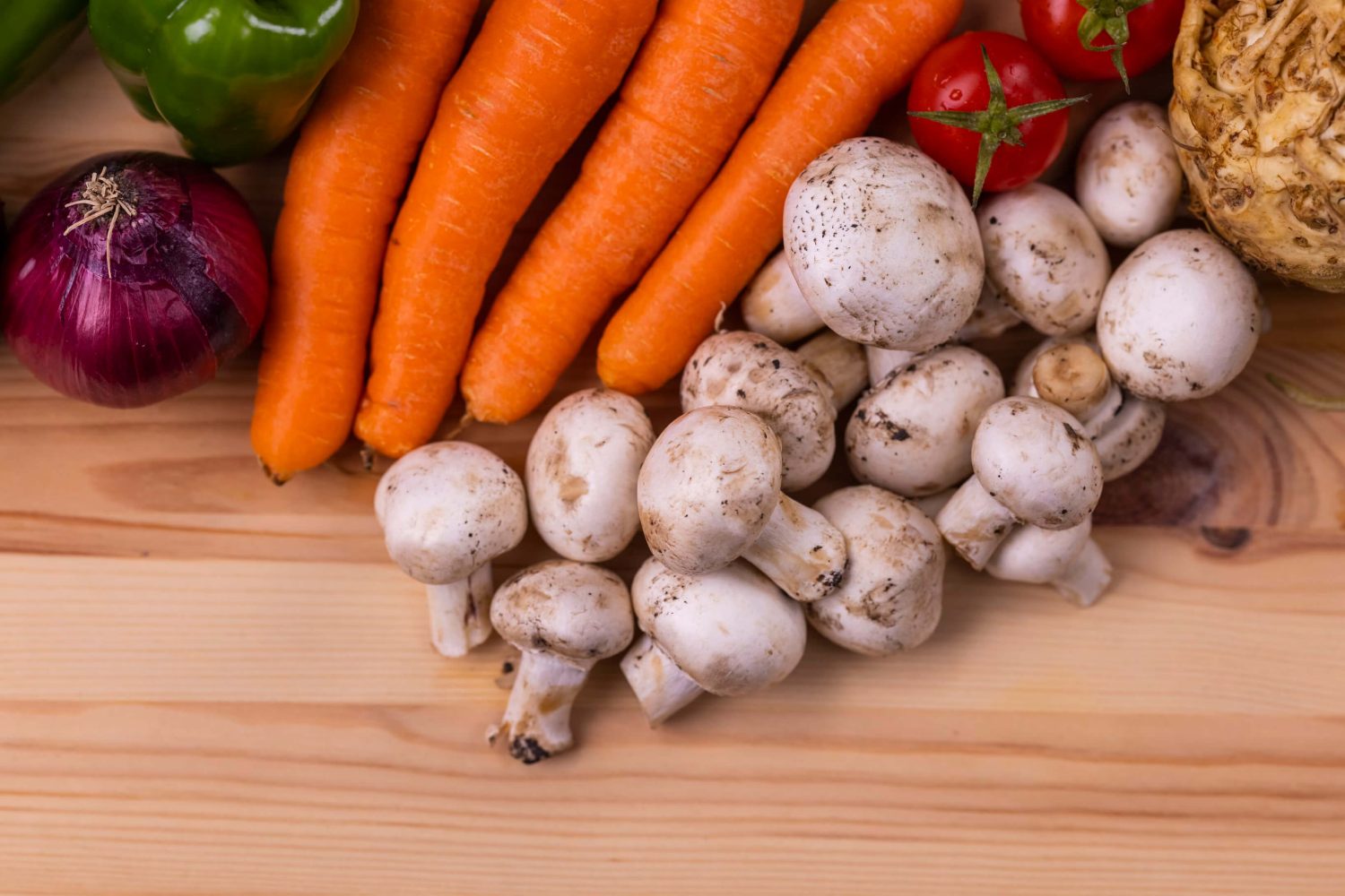 Eine Zwiebel, Möhren, Pilze, Tomaten und mehr Gemüse liegen nebeneinander