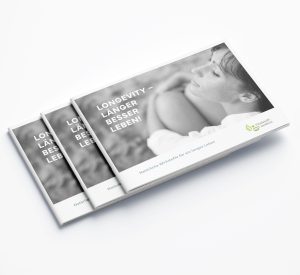 Drei gestapelte Broschüren "Broschüre - Longevity Broschüre" zeigen eine lächelnde Frau auf dem Umschlag mit der Überschrift "LÄNGER BESSER LEBEN!". In der rechten unteren Ecke erscheint ein grünes Blatt-Logo.
