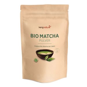 In einem beigen, wiederverschließbaren Beutel mit der Aufschrift Matcha Pulver Bio befindet sich eine Schale mit grünem Matcha-Pulver mit Blättern, die den Bio-Matcha aus Japan hervorheben - perfekt für alle, die Matcha Pulver kaufen möchten.