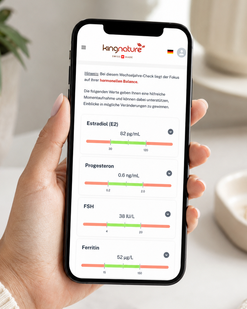 Eine Hand hält ein Smartphone, auf dem in der Kingnature-App die Ergebnisse der Hormontests für Östradiol, Progesteron, FSH und Ferritin angezeigt werden – ideal für einen Wechseljahre-Check zu Hause. Im Hintergrund sind eine Pflanze, ein Notizbuch und eine Vase verschwommen zu sehen.