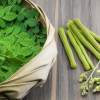 Ein Korb mit frischen grünen Moringa-Blättern, -Schoten und -Blüten steht auf Holz – eine schöne Präsentation für alle, die Bio-Moringa-Blattpulver suchen.