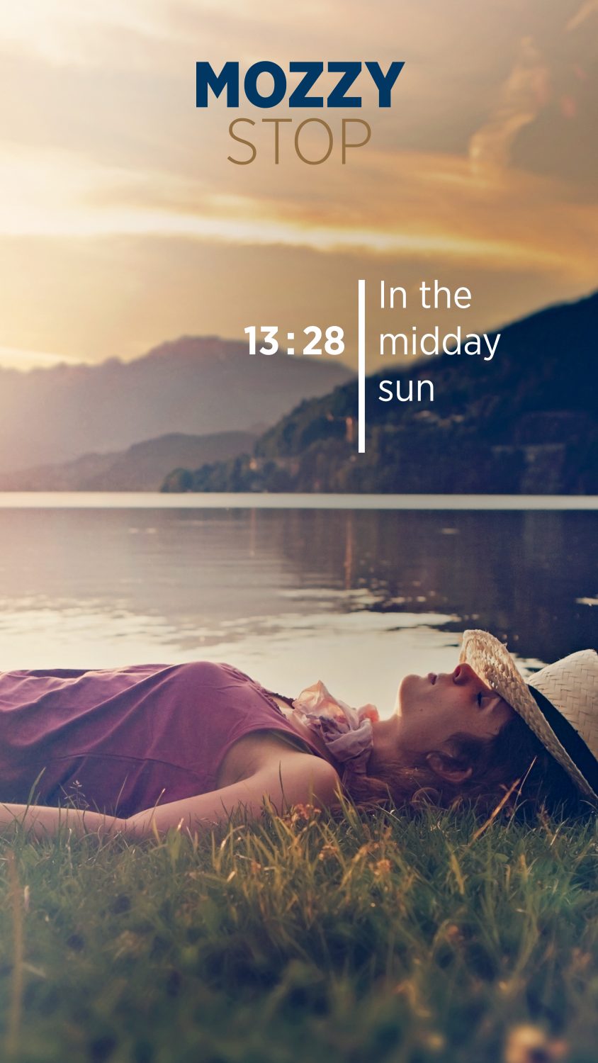 Eine Person, die einen Sonnenhut trägt, entspannt sich im Gras an einem ruhigen See mit Bergen und einem Sonnenuntergangshimmel im Hintergrund. Das Bild zeigt das MozzyStop-Logo, die Uhrzeit 13:28 und den Satz "In der Mittagssonne.