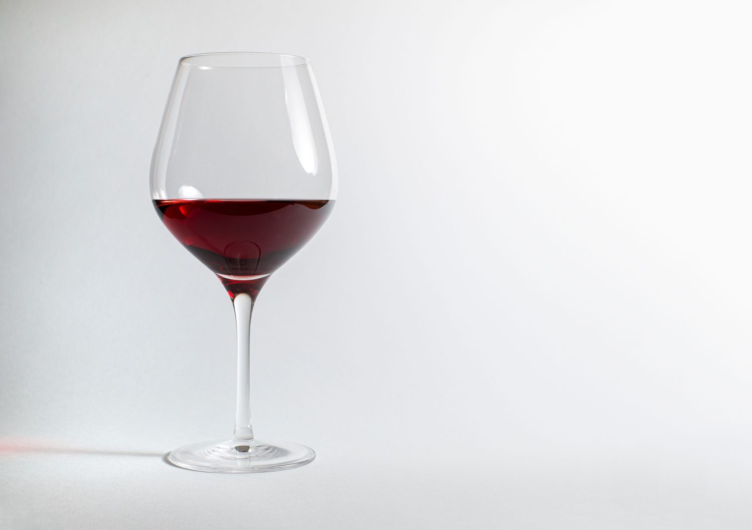 Ein klares Weinglas, das zur Hälfte mit Rotwein gefüllt ist, steht vor einem schlichten, hellen Hintergrund mit viel Freiraum auf der rechten Seite – ideal, um über Ernährung zu sprechen oder die mit dem Weinkonsum verbundenen Symptome einer Histaminintoleranz zu erörtern.