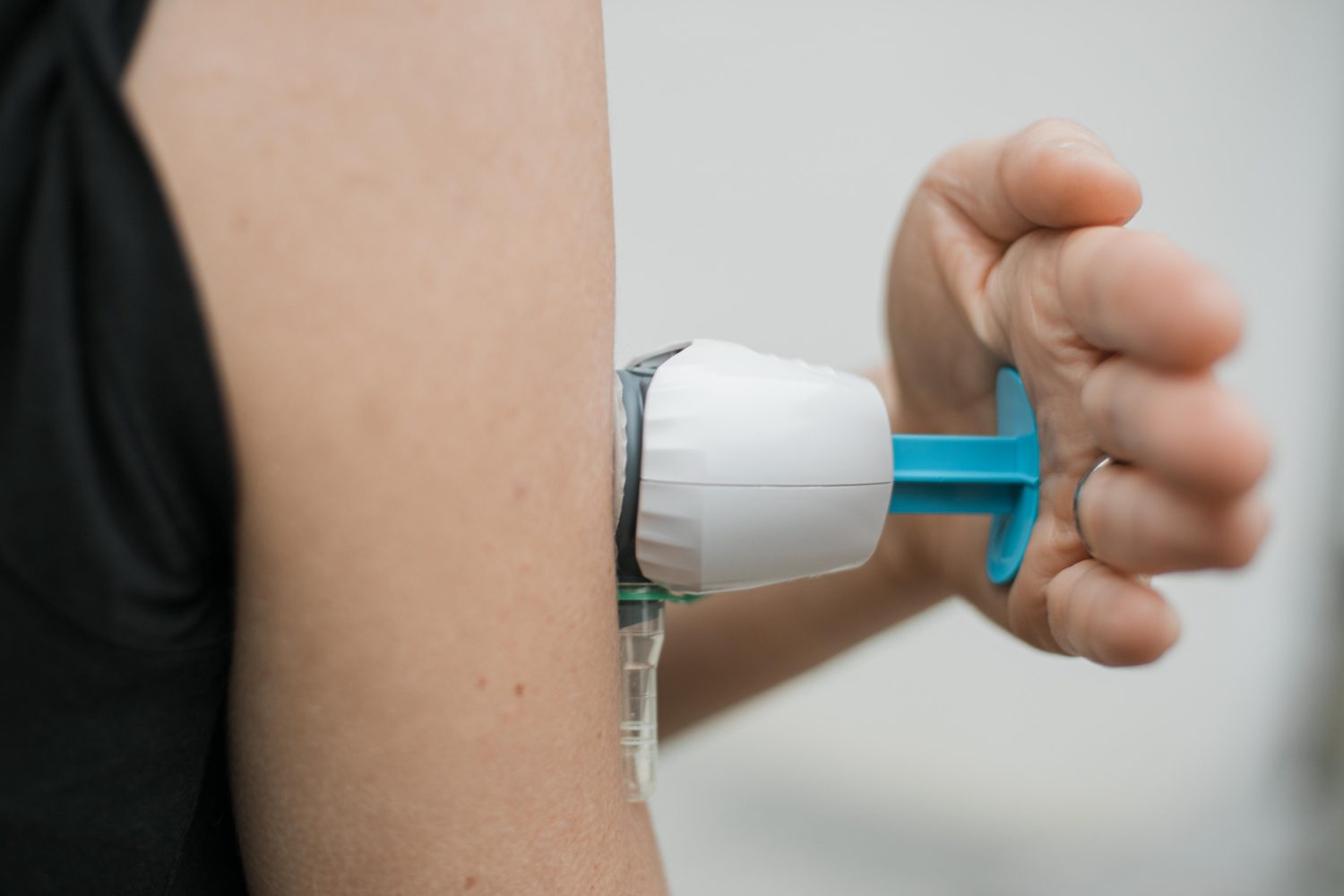 Eine Person verwendet einen Autoinjektor am Oberarm und drückt mit dem Daumen auf den blauen Kolben. Dieses Verfahren ähnelt dem TAP-Blut-Test Blei-Check, da beide Substanzen durch die Haut verabreicht werden.