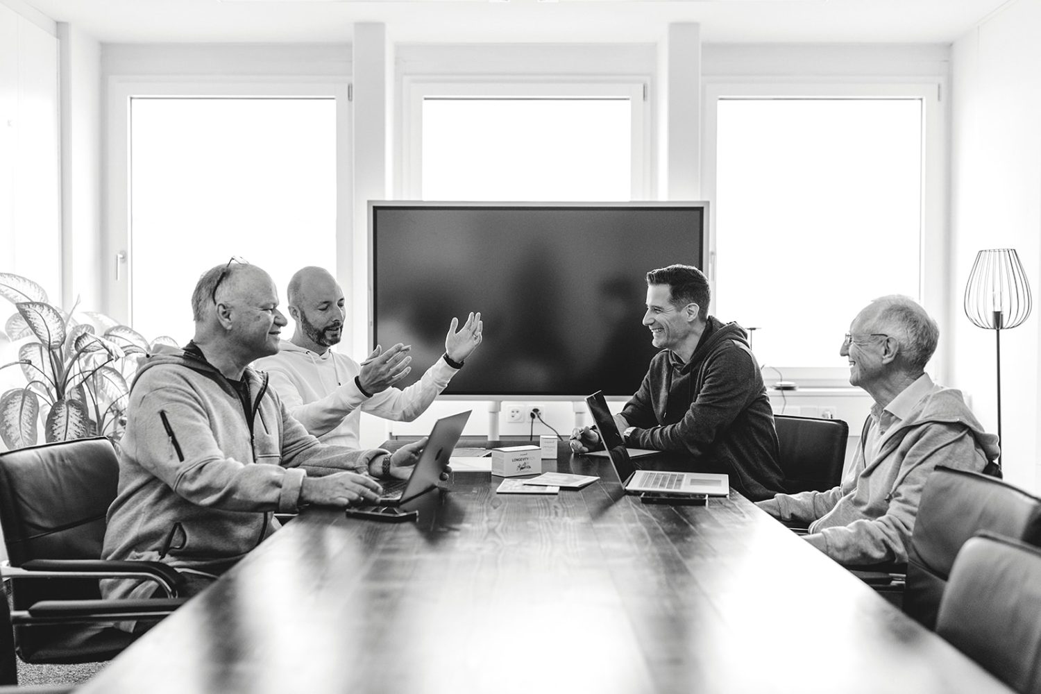 Vier Männer, möglicherweise Mitglieder des kingnature-Verwaltungsrats, sitzen mit Laptops um einen langen Konferenztisch und diskutieren in einem hellen Büro mit großen Fenstern und einem Fernsehbildschirm. Die Atmosphäre wirkt kooperativ und professionell.