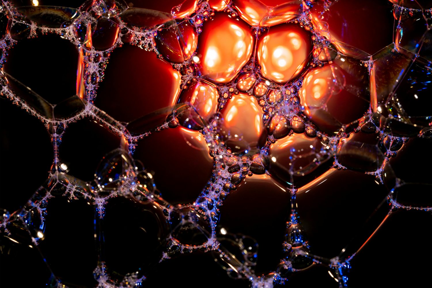 Nahaufnahme von Seifenblasen, die von orangefarbenem und rotem Licht durchleuchtet werden, wodurch ein lebendiges, abstraktes Muster vor einem dunklen Hintergrund entsteht - ein Bild, das an die dynamische Energie von Vitamin B12 erinnert.
