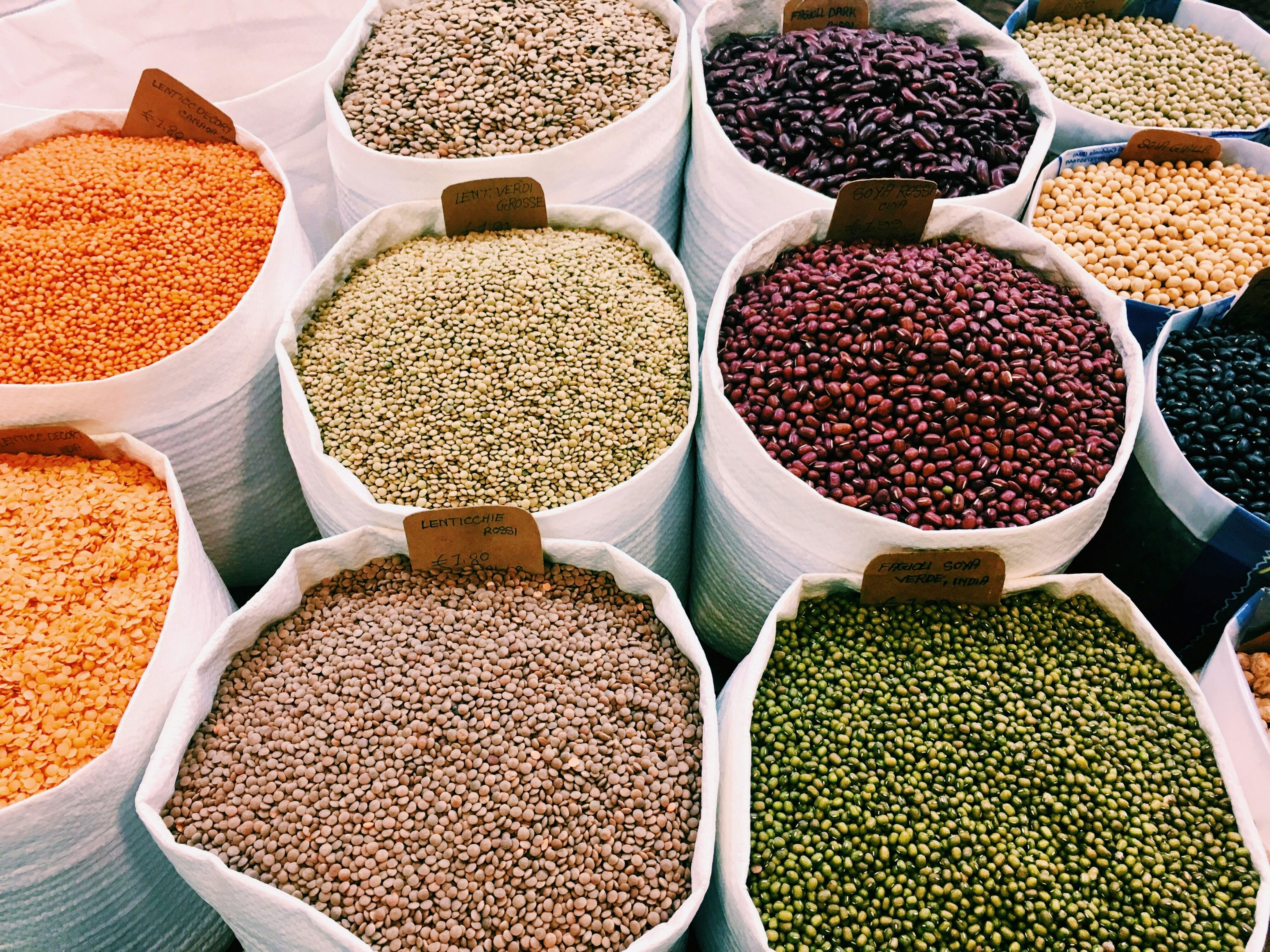De grands sacs blancs de haricots Cholin Vida et de lentilles séchées colorées - orange, vert, marron, noir et rouge - sont exposés sur un marché, chaque variété bien étiquetée.