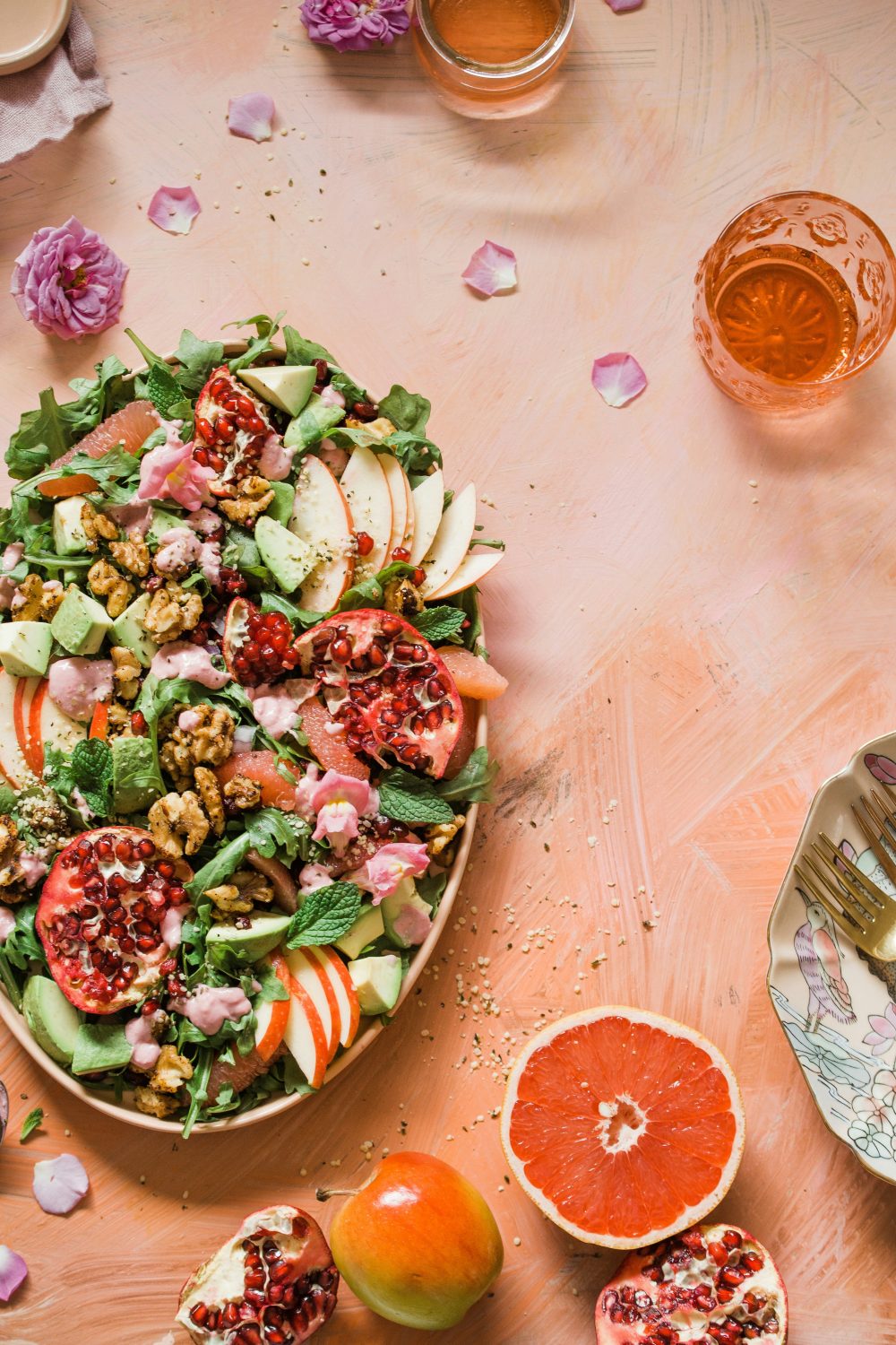 Ein bunter Salat mit Apfelscheiben, Avocado, Walnüssen, Granatapfelkernen, Gemüse und rosa Dressing wird auf einer ovalen Platte serviert – perfekt für alle, die ihre Gesundheitskosten mit frischen Zutaten und lebendigen Aromen senken möchten.