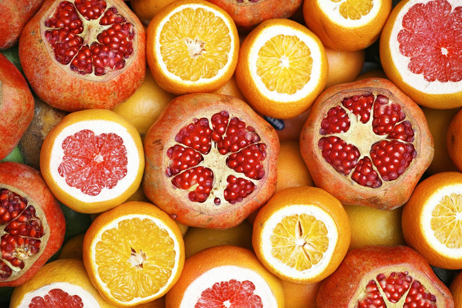 Eine bunte Auswahl halbierter Granatäpfel, Grapefruits und Orangen, dicht beieinander angeordnet, sodass ihr leuchtend rotes, orangefarbenes und gelbes Inneres voller Vitamin C zur Schau gestellt wird.