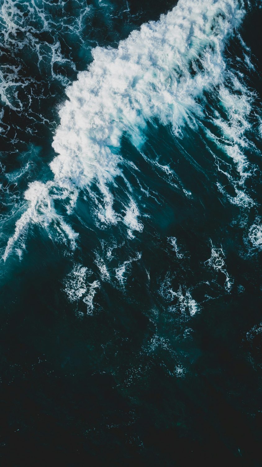 Luftaufnahme von Meereswellen, die über tiefes, dunkelblaues Wasser rauschen und weißen Schaum verbreiten - ein Tanz der Natur, der die Reinheit von Omega-3-Fettsäuren widerspiegelt.