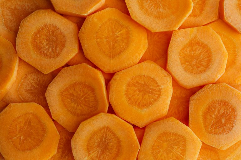 Nahaufnahme mehrerer überlappender orangefarbener Karottenscheiben, die ihre kreisförmige Form und die strahlenförmigen Muster in der Mitte hervorheben, frisch und lebendig.