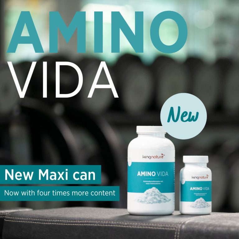 Zwei Flaschen Amino Vida Maxi-Dose Presslinge stehen auf einem Fitnessgerät, eine große, eine kleine. Text: Neue Maxi-Dose – jetzt mit viermal mehr Inhalt. Im Hintergrund sind Fitnessgeräte unscharf dargestellt.