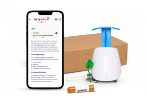 Ein Smartphone, das zeigt, wie man den Bleigehalt misst, liegt neben dem TAP-Blutanalyse Blei-Check-Kit: ein weiß-blauer Handpumpen-Wasserfilter, eine Pappschachtel, ein grünes Ventil und eine kleine orangefarbene Probenflasche.