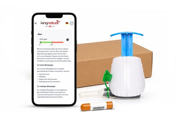 Ein Smartphone, das zeigt, wie man den Bleigehalt misst, liegt neben dem TAP-Blutanalyse Blei-Check-Kit: ein weiß-blauer Handpumpen-Wasserfilter, eine Pappschachtel, ein grünes Ventil und eine kleine orangefarbene Probenflasche.