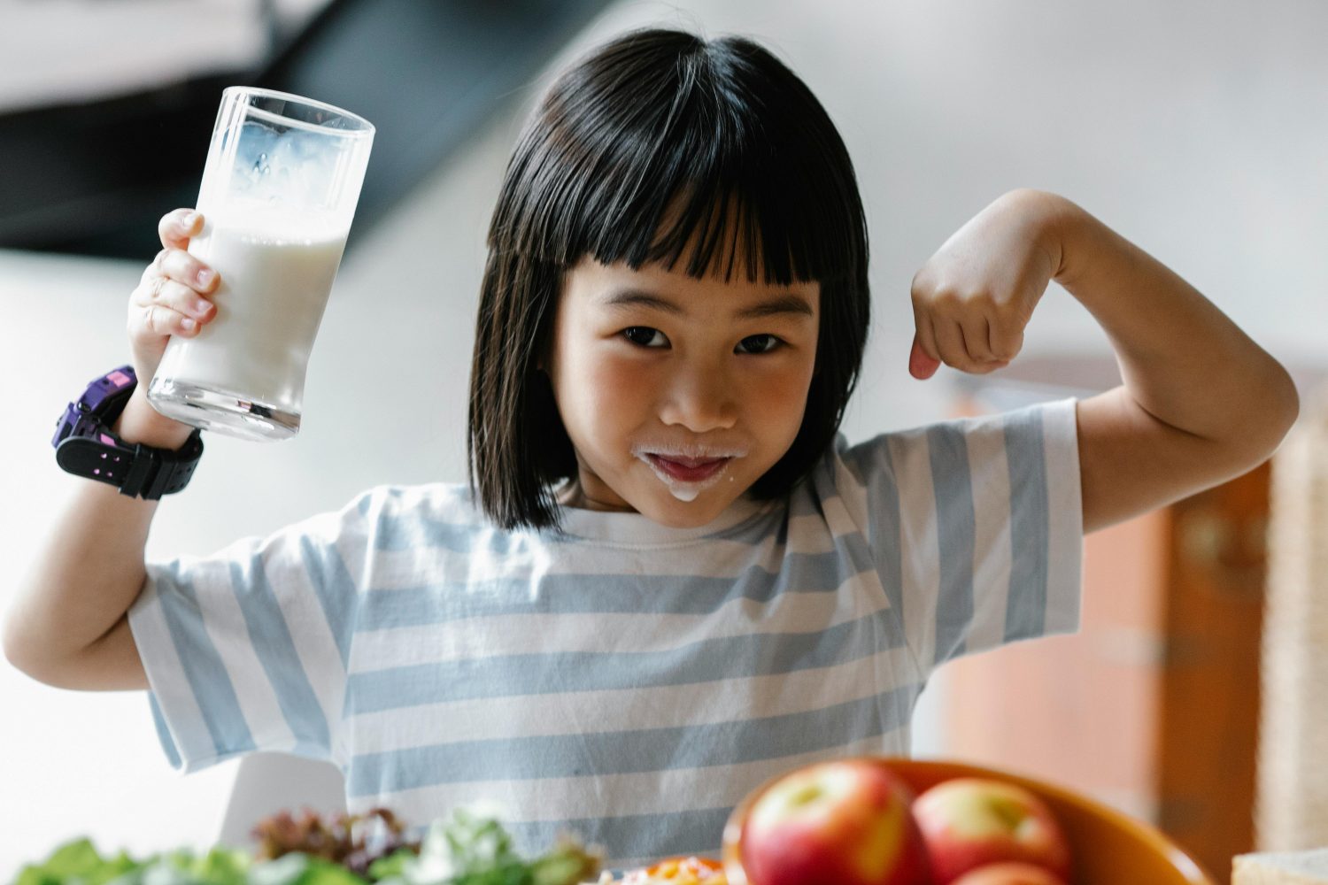 Ein kleines Mädchen trinkt Milch und zeigt, dass sie stark ist