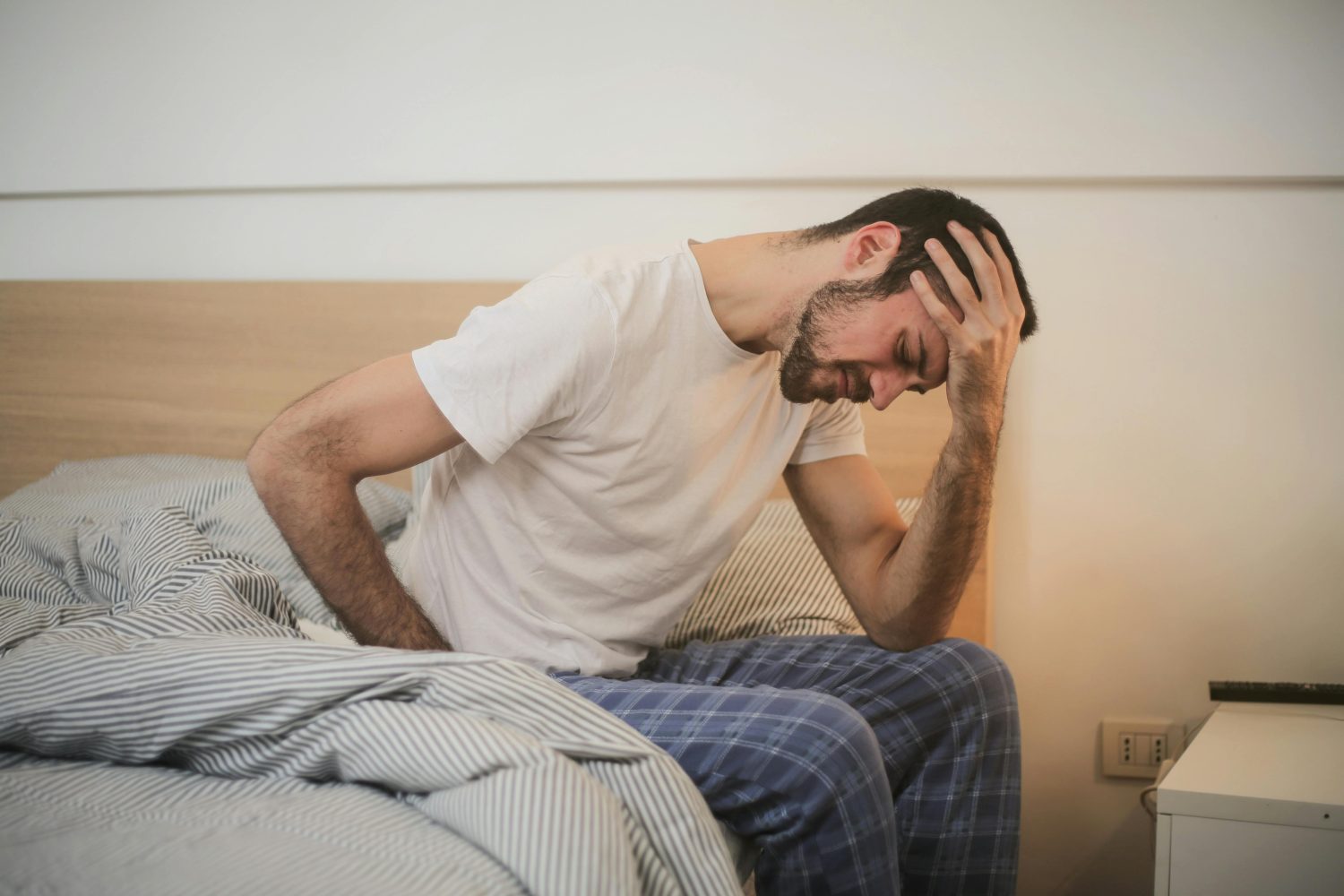 Ein junger Mann sitzt im Bett und hält sich müde den Kopf