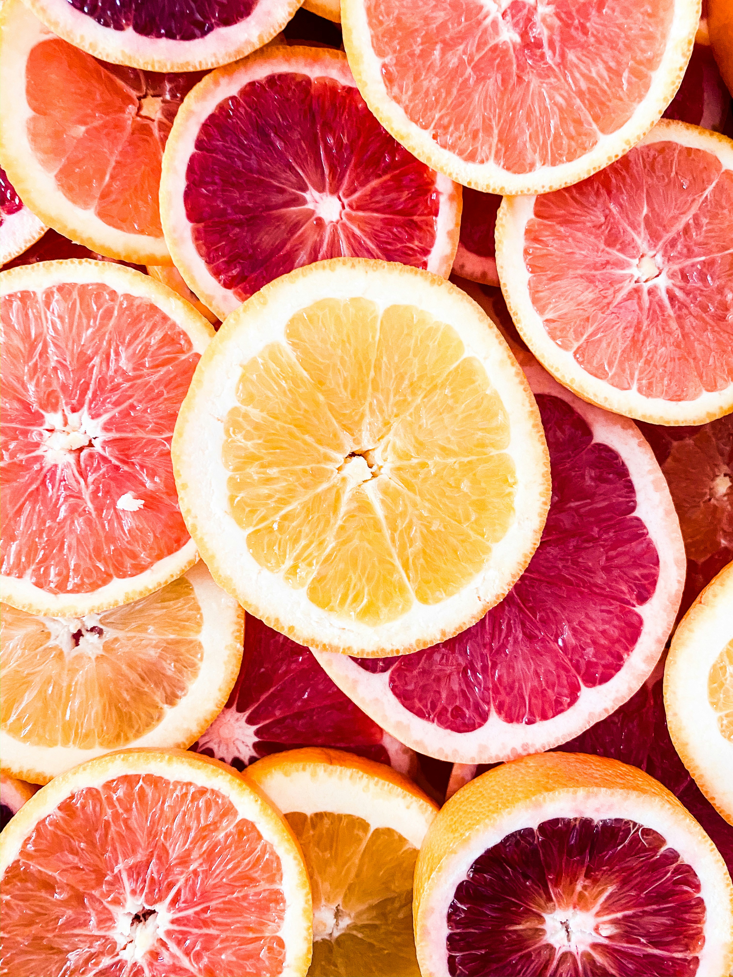 Un primo piano di varie fette di agrumi, tra cui arance, pompelmi e arance rosse, mostra i colori vivaci del giallo, del rosa e del rosso: l'ispirazione perfetta per chi ama l'essenza rinfrescante dell'olio di pompelmo.