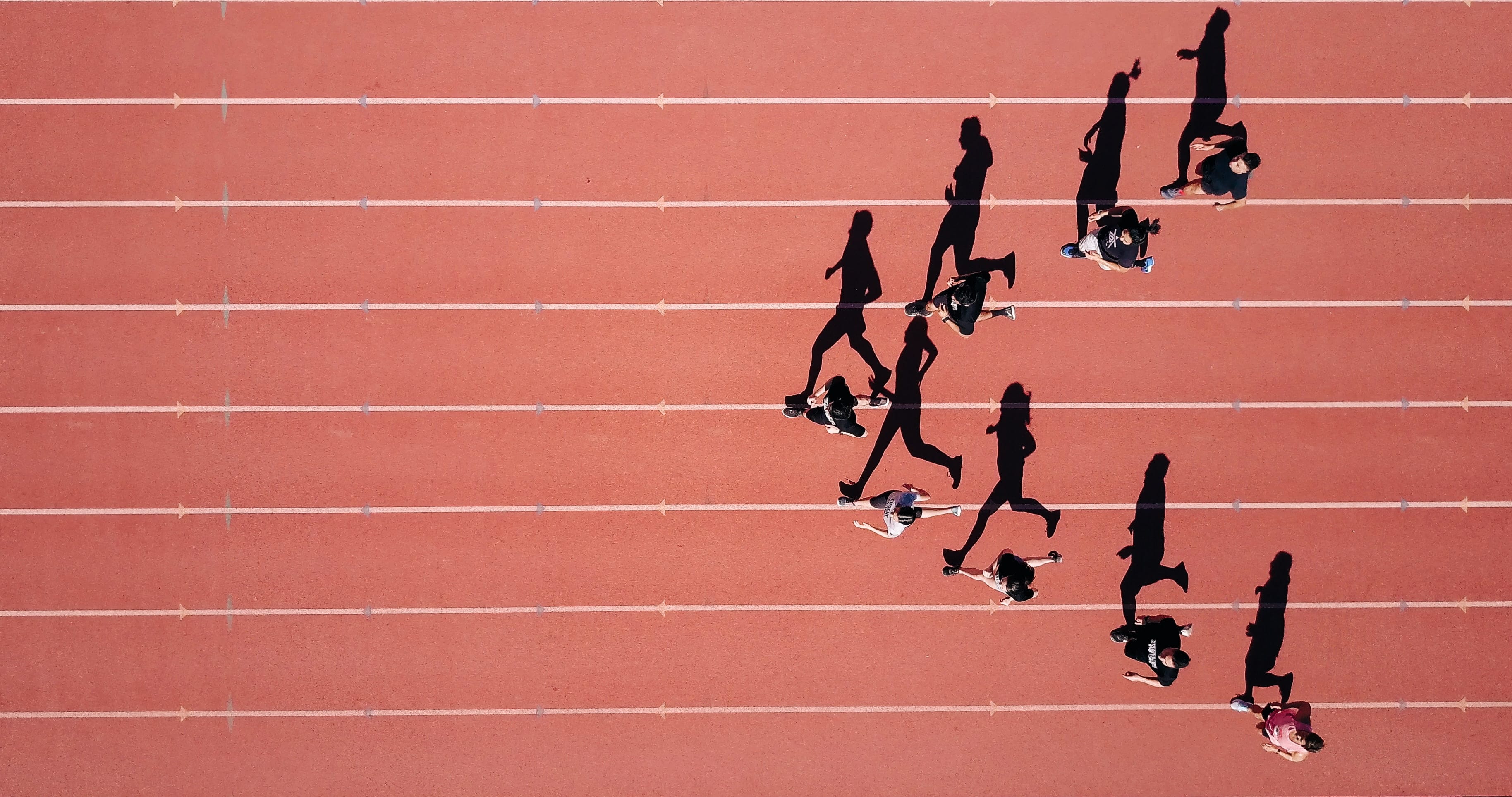 A group of people walking on a red outer track, casting long shadows across the lanes, as seen from above—a reflection of safety and transparency, just like the products on the Cologne List that have been tested.