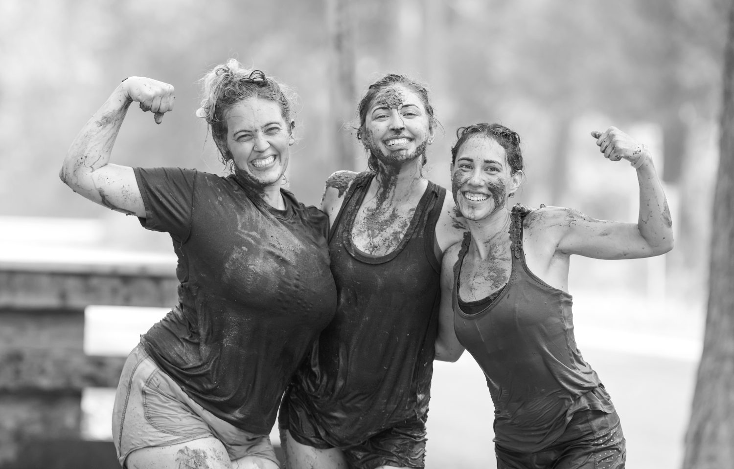 Drei Frauen, die lächelnd ihre Arme bewegen, während sie im Freien mit Schlamm bedeckt sind, strahlen Freude und Kameradschaft aus - sie fangen den Geist der Ermächtigung ein, der für Broschüren - Wechseljahre ideal ist.